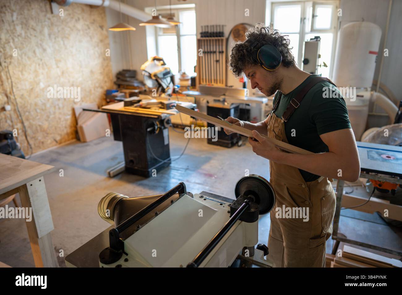 Bricoleur professionnel sérieux mesure l'épaisseur de la planche de bois avec des étriers dans l'atelier de meubles Banque D'Images
