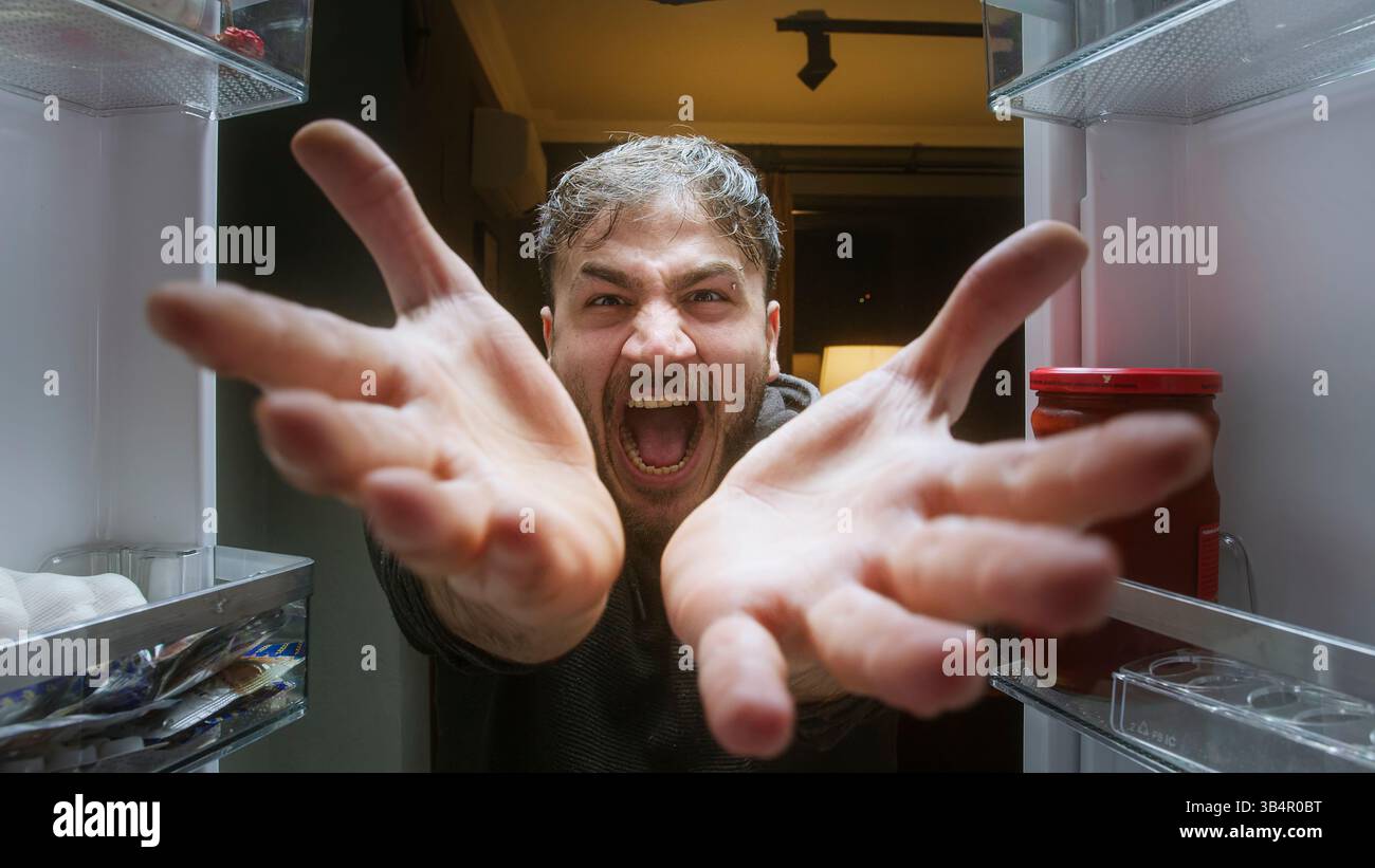 Homme affamé en colère criant avec les mains vides à l'intérieur du réfrigérateur du point de vue du réfrigérateur Banque D'Images