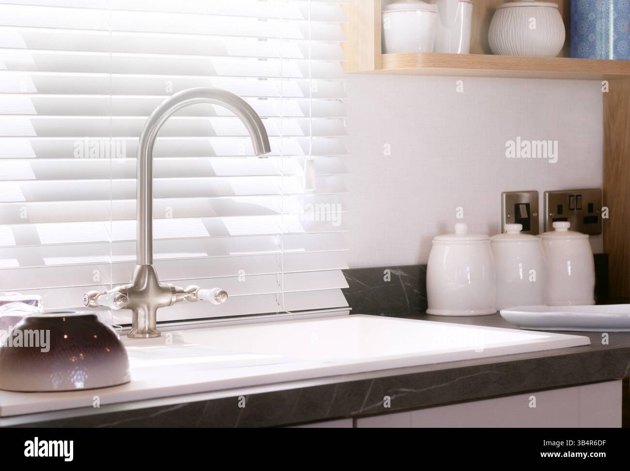 Intérieur de cuisine avec évier et comptoir en marbre. Encastrement de lavabo surmonté intégré avec robinet en nickel brossé. Stores de fenêtre au toucher traditionnel. Banque D'Images