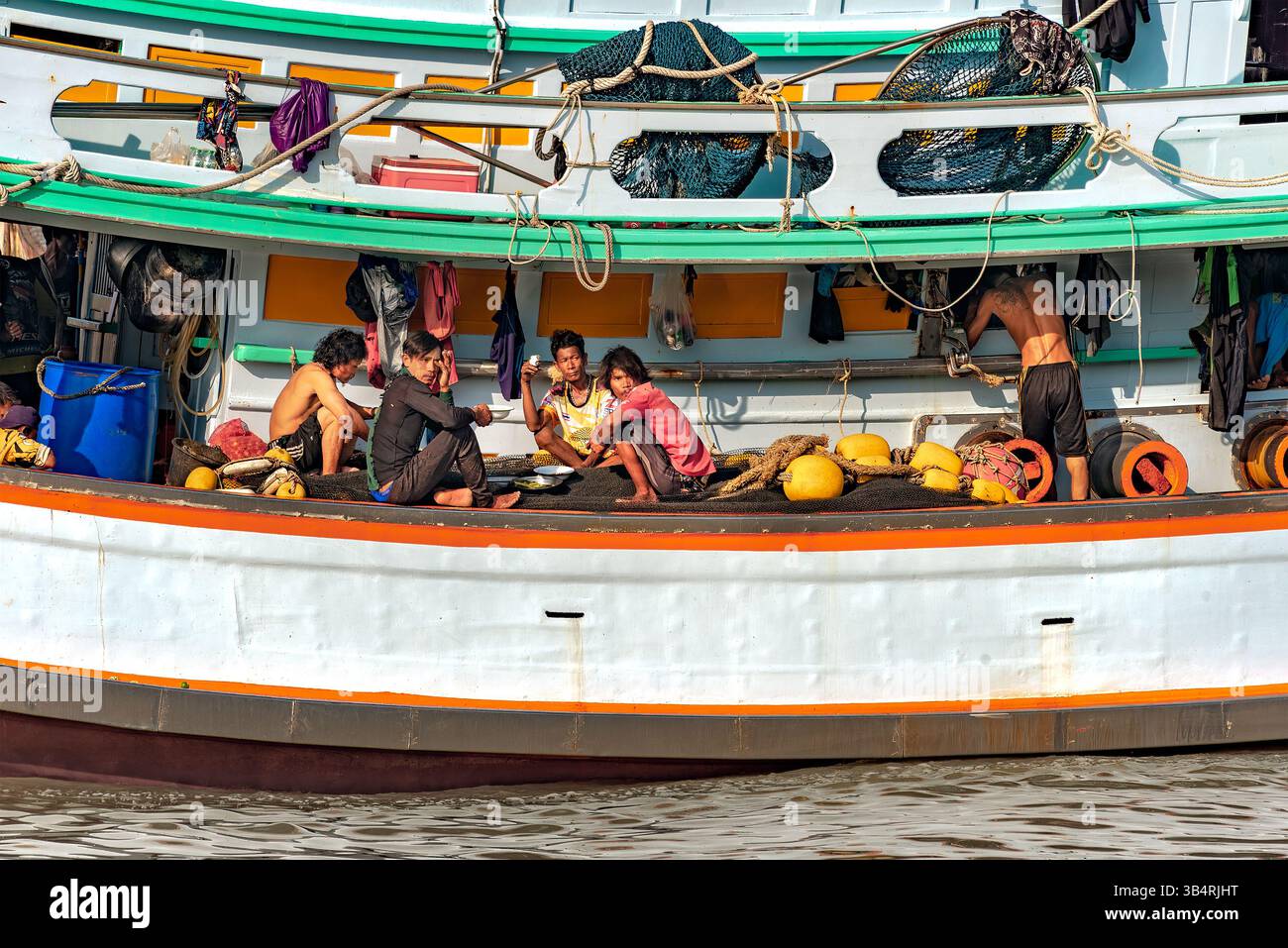 Rayong, Thaïlande, le 26 octobre 2024 : un groupe de travailleurs sur un bateau de pêche déjeunent, tandis qu’un autre est debout et travaille. Banque D'Images