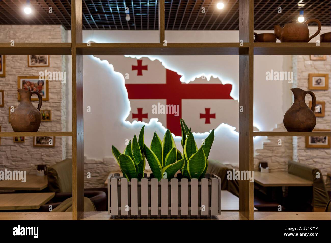 Restaurant confortable avec des pichets traditionnels en argile, des plantes vertes, des étagères en bois, et une carte du drapeau géorgien brillant sur un mur texturé Banque D'Images