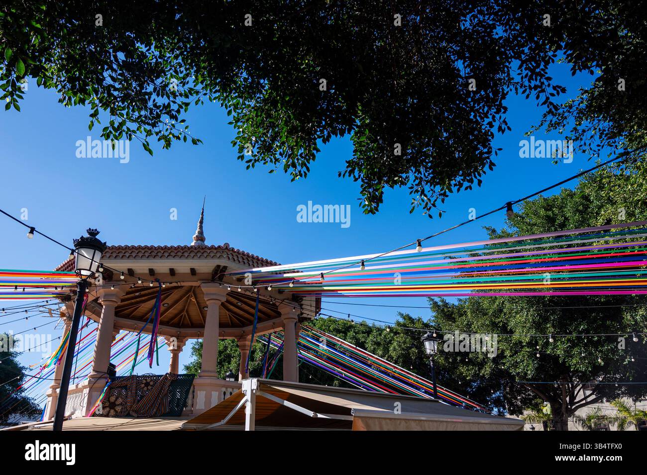 Une tente colorée est installée dans un parc avec un ciel bleu au-dessus. La tente est décorée de rubans et de cordes colorés, créant une atmosphère festive Banque D'Images