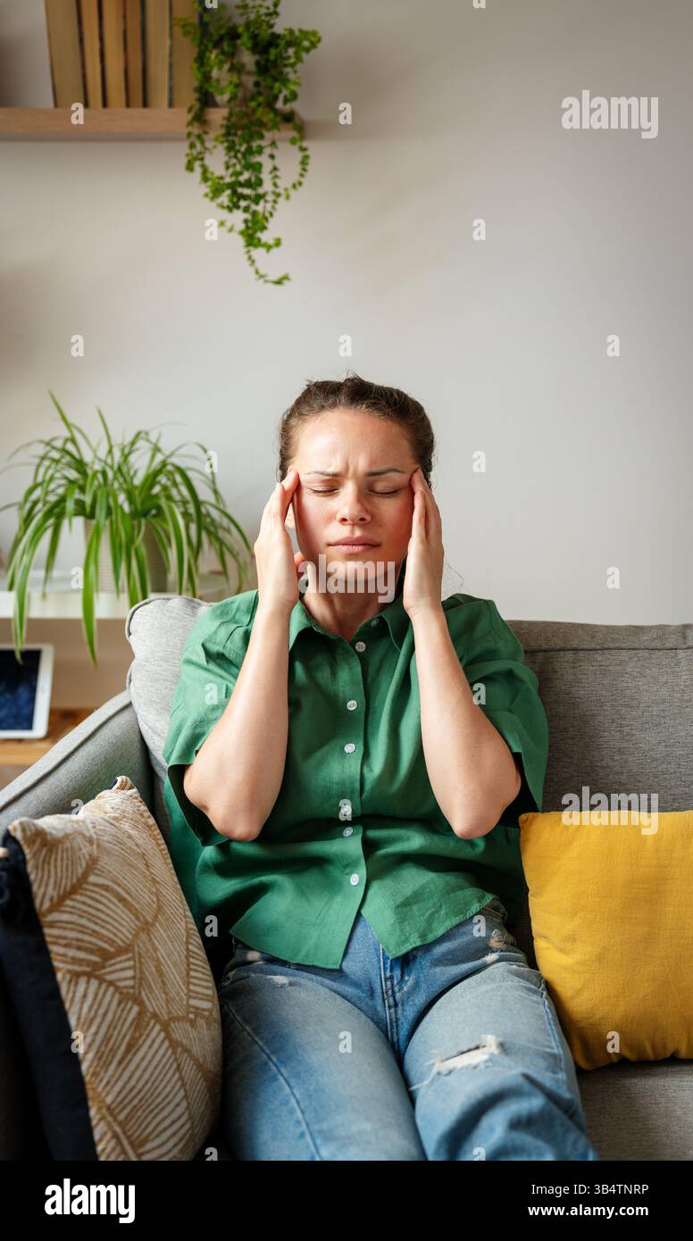Femme caucasienne assise sur un canapé avec la tête dans les mains souffrant de maux de tête à la maison Banque D'Images