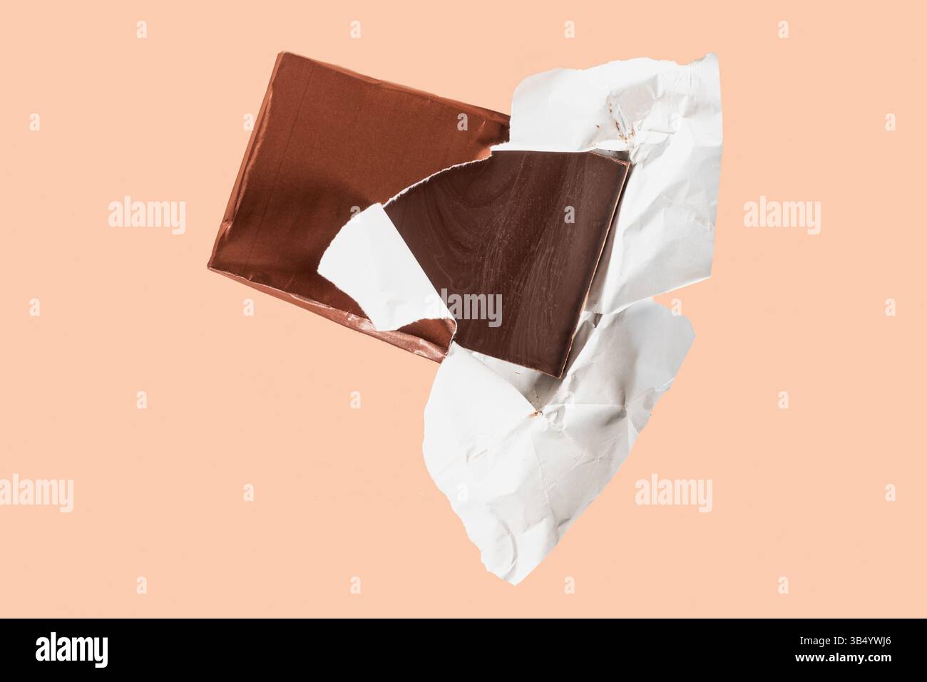 Barre de chocolat noir artisanale avec emballage partiellement ouvert, révélant la moitié du chocolat, fond couleur saumon. Banque D'Images
