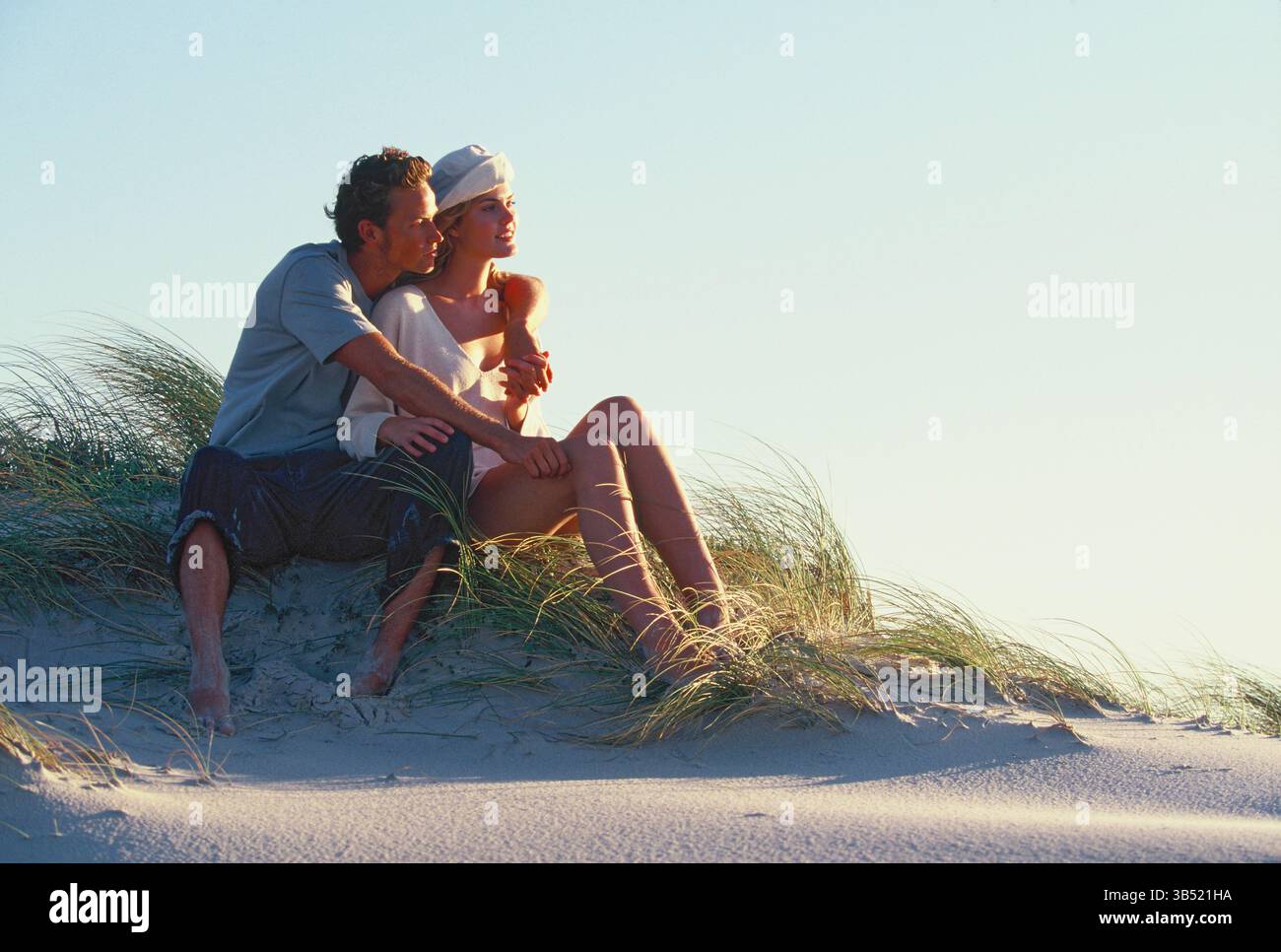 Jeune couple romantique assis sur une dune de sable à la plage. Banque D'Images