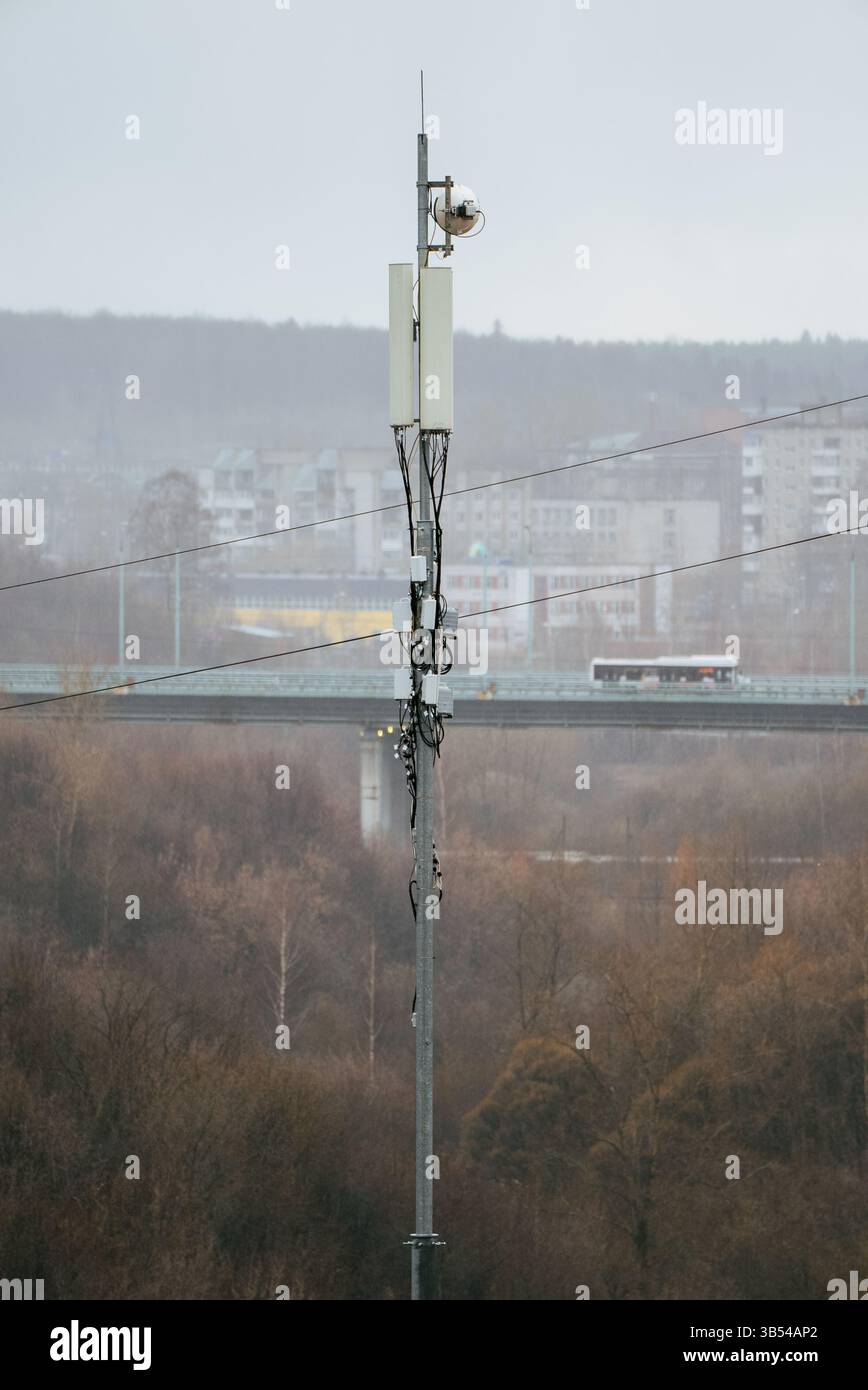 Tour de station de base cellulaire avec antennes et antenne parabolique à micro-ondes fournissant des services de communication sans fil dans un environnement urbain brumeux, avec un pont et des bâtiments en arrière-plan Banque D'Images