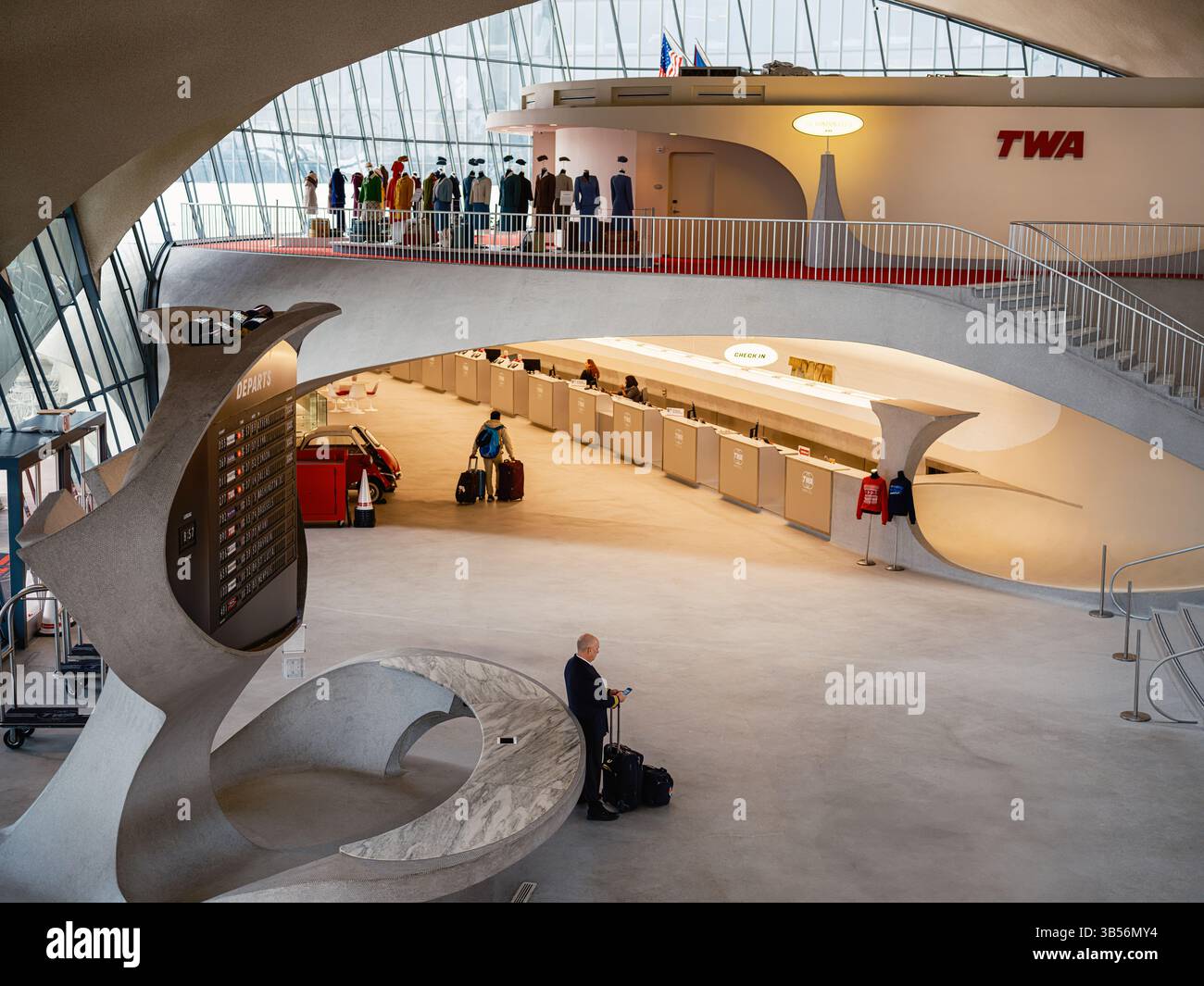Image éditoriale à l'intérieur de l'hôtel TWA à l'aéroport JFK, New York. Un pilote se tient près du panneau des départs pendant que les voyageurs marchent pour s'enregistrer. TWA unifor Banque D'Images Image éditoriale à l'intérieur de l'hôtel TWA à l'aéroport JFK, New York. Un pilote se tient près du panneau des départs pendant que les voyageurs marchent pour s'enregistrer. TWA unifor Banque D'Images