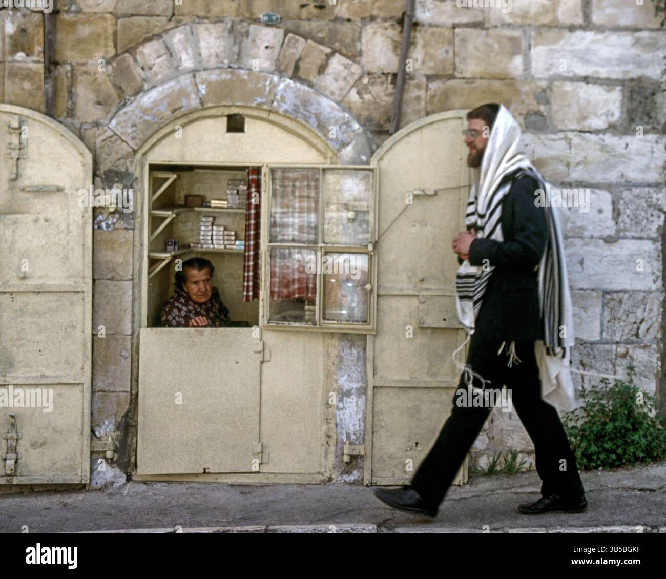 8 avril 1988, Jérusalem, Israël : un juif israélien orthodoxe barbu, portant un yarmulke (chapeau de crâne) et un tallis traitional (châle de prière) marche devant un stand à cigarettes à Jérusalem. (Crédit image : © Arnold Drapkin/ZUMA Press Wire) Banque D'Images