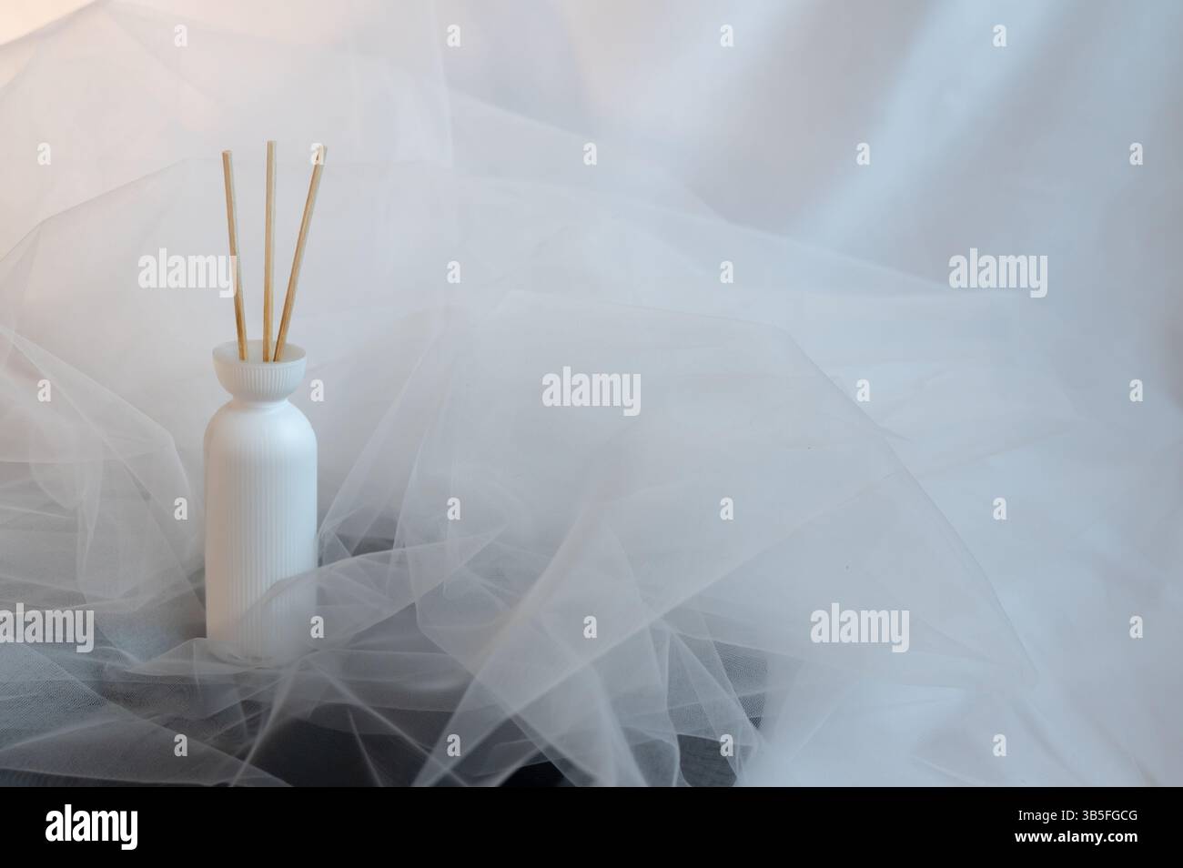 Un beau vase blanc rempli de bâtons fins est élégamment affiché sur un tissu doux et blanc qui complète parfaitement son apparence Banque D'Images