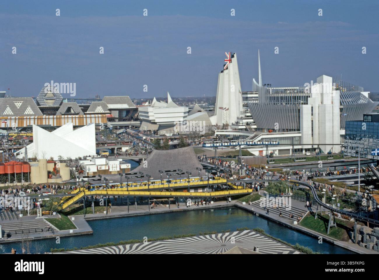 Une vue de l'Expo 67, Montréal, Québec, Canada en 1967. Le pavillon de la Grande-Bretagne est au centre droit. L'architecte britannique Sir Basil Spence a conçu le pavillon, qui utilisait des charpentes en acier et des feuilles d'amiante. La tour était surmontée d'un drapeau de l'union Jack 3D. À droite se trouve le pavillon français – une grande structure en béton et en acier était enveloppée de hautes ailettes en aluminium. Le site du système de transport surélevé était un monorail à 3 boucles appelé le Minirail - une photographie vintage des années 1960. Banque D'Images