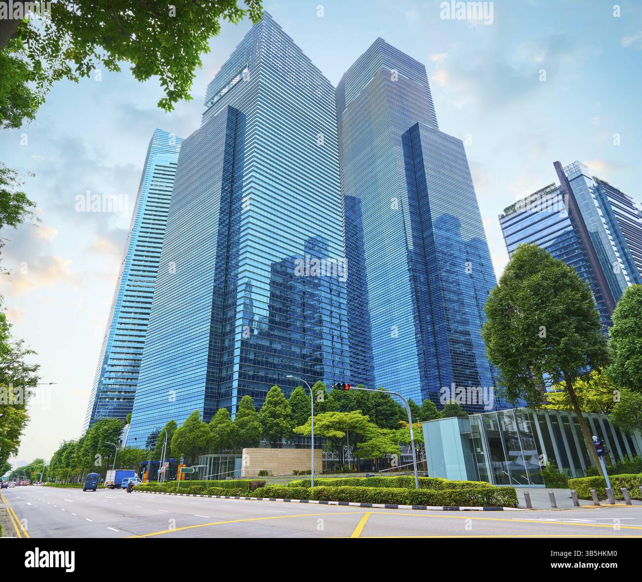 Gratte-ciel en verre s'élevant dans un quartier d'affaires urbain avec des arbres verts, mettant en valeur l'architecture moderne et le développement durable de la ville Banque D'Images
