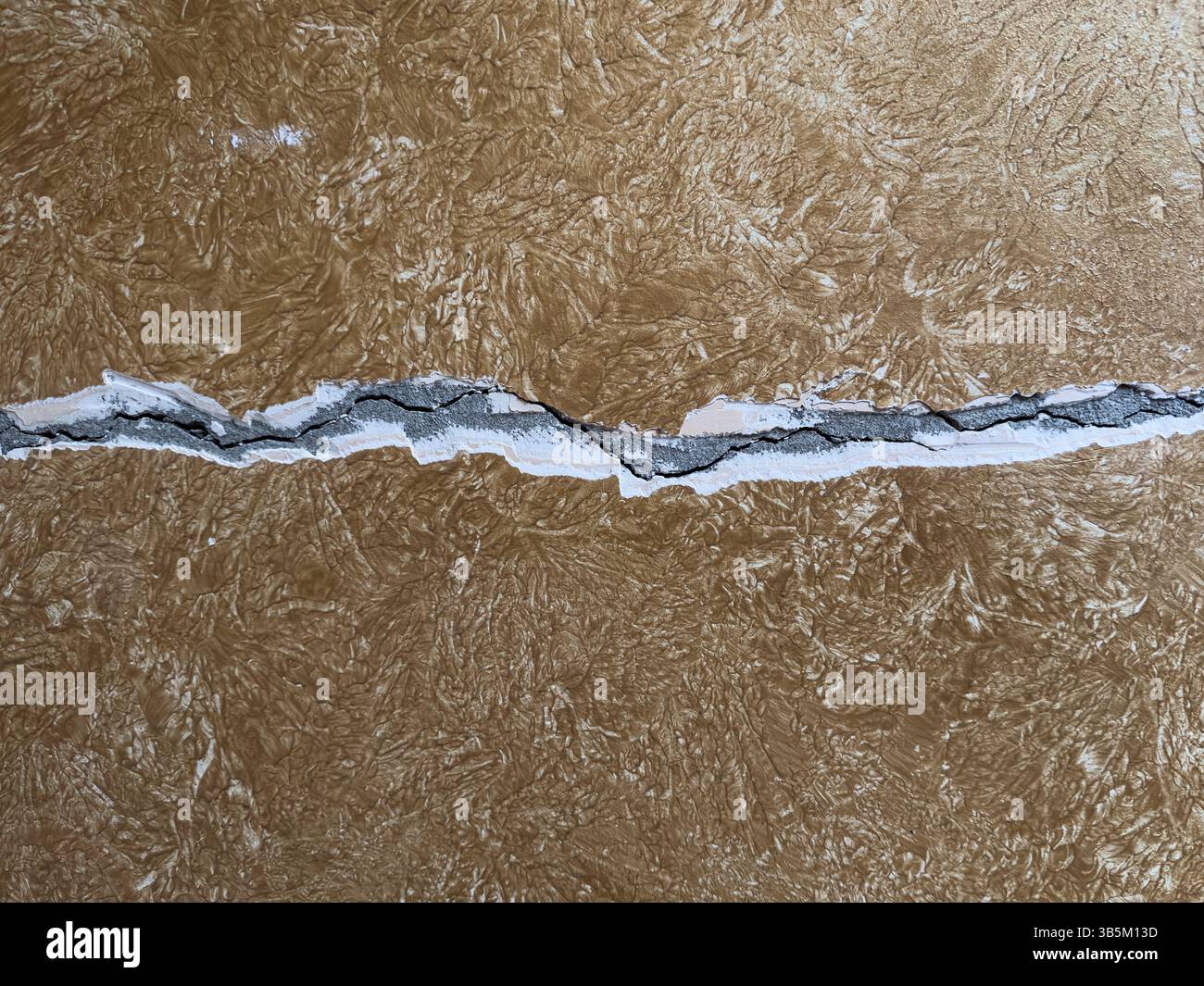 Fissure murale horizontale à travers la surface de plâtre texturé brun. Vue rapprochée des dommages, détail abstrait, personne, symbole de faiblesse ou d'échec. Banque D'Images