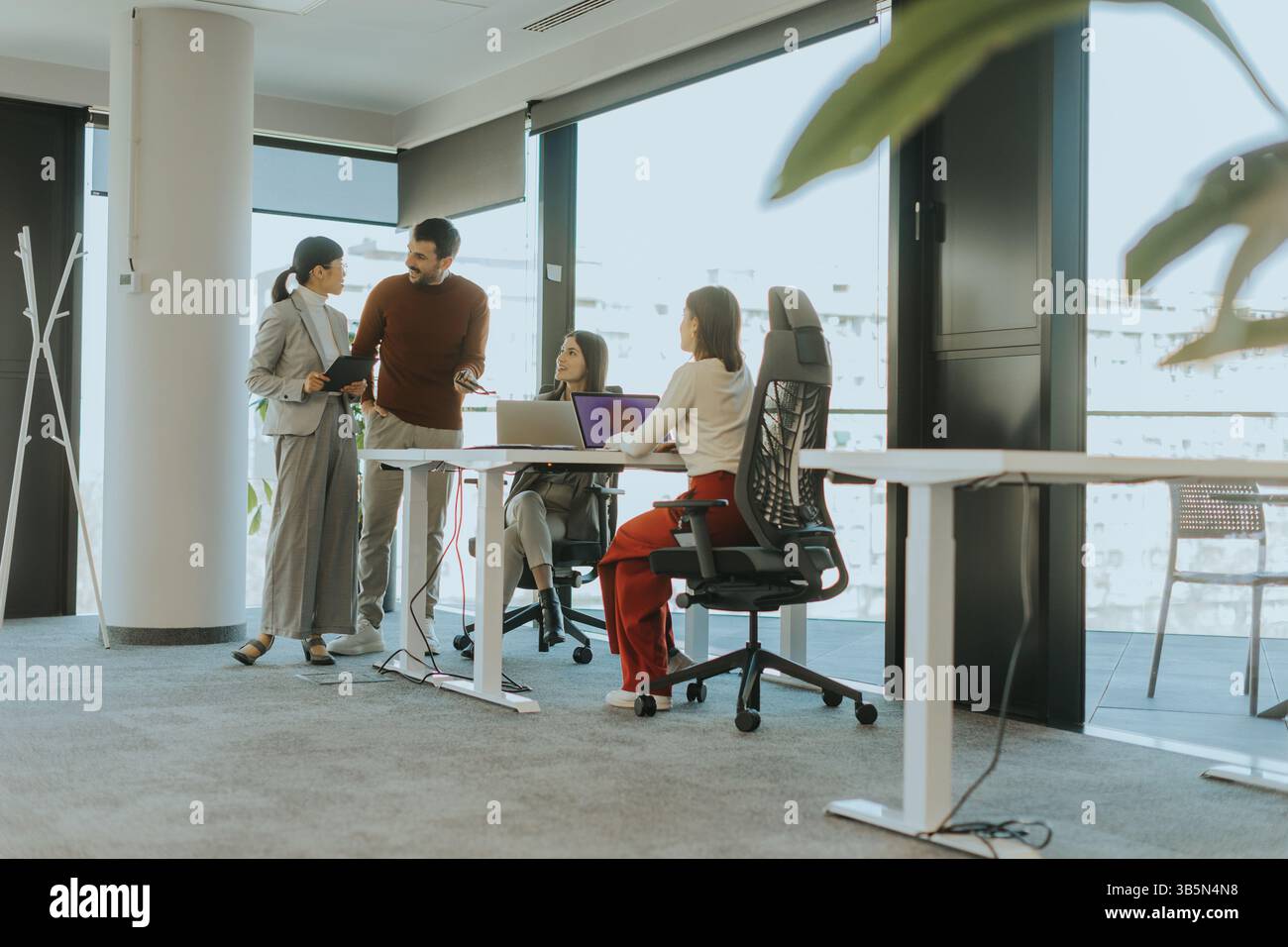 Les collègues se réunissent dans un bureau spacieux et lumineux, ce qui améliore la collaboration. Une réunion d'idées fleurit alors qu'un membre partage ses idées, entouré de foc Banque D'Images