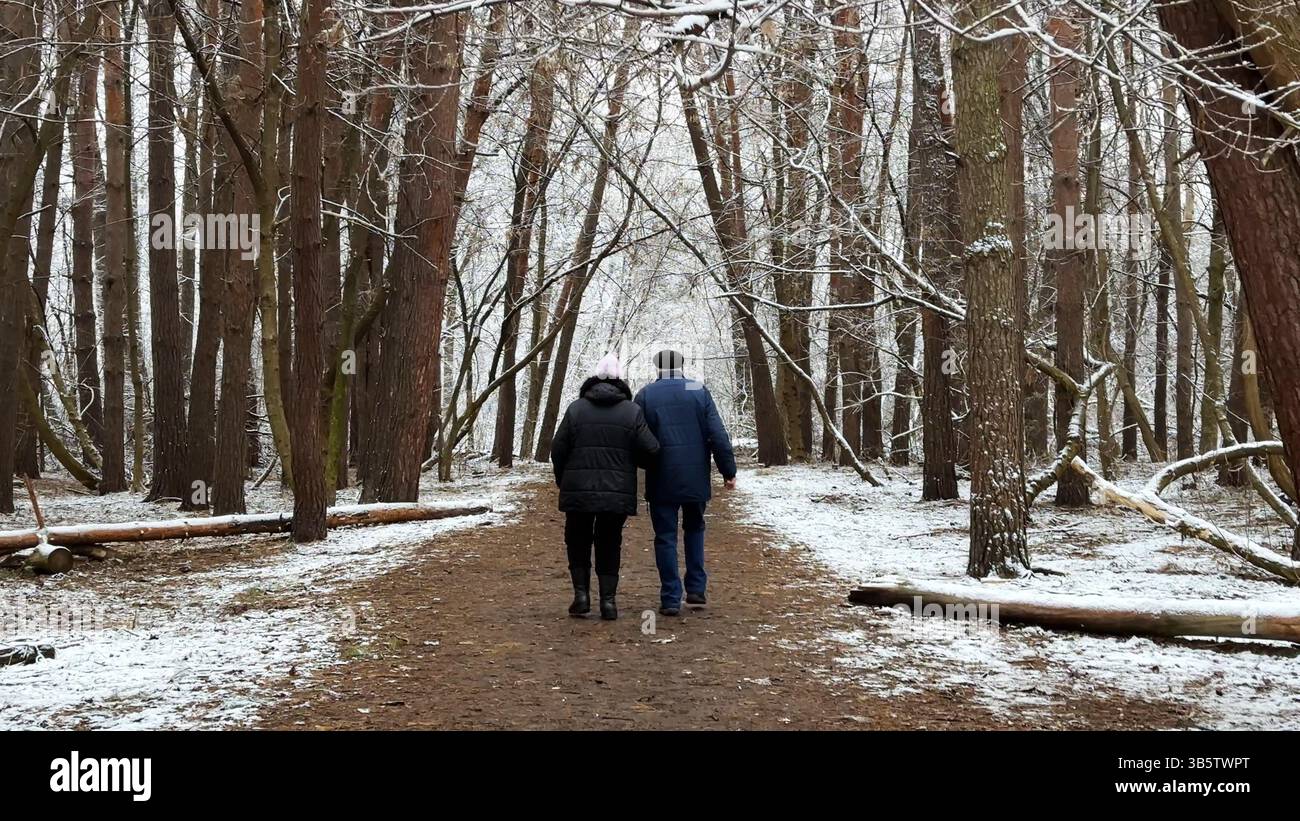 Couple mûr allant sur le chemin enneigé à la forêt de pins d'hiver. Mari senior et femme marchant à travers le sentier dans la forêt de conifères. Ancienne paire de Banque D'Images