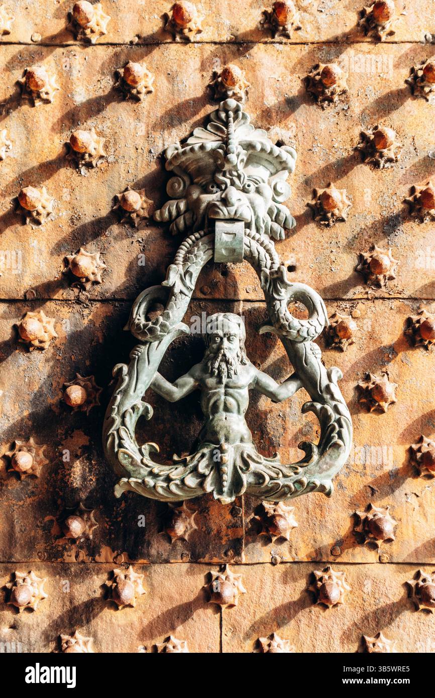 Frappeur de porte en bronze orné avec figure mythologique sur porte médiévale en bois cloutée dans le centre historique de Gênes Banque D'Images