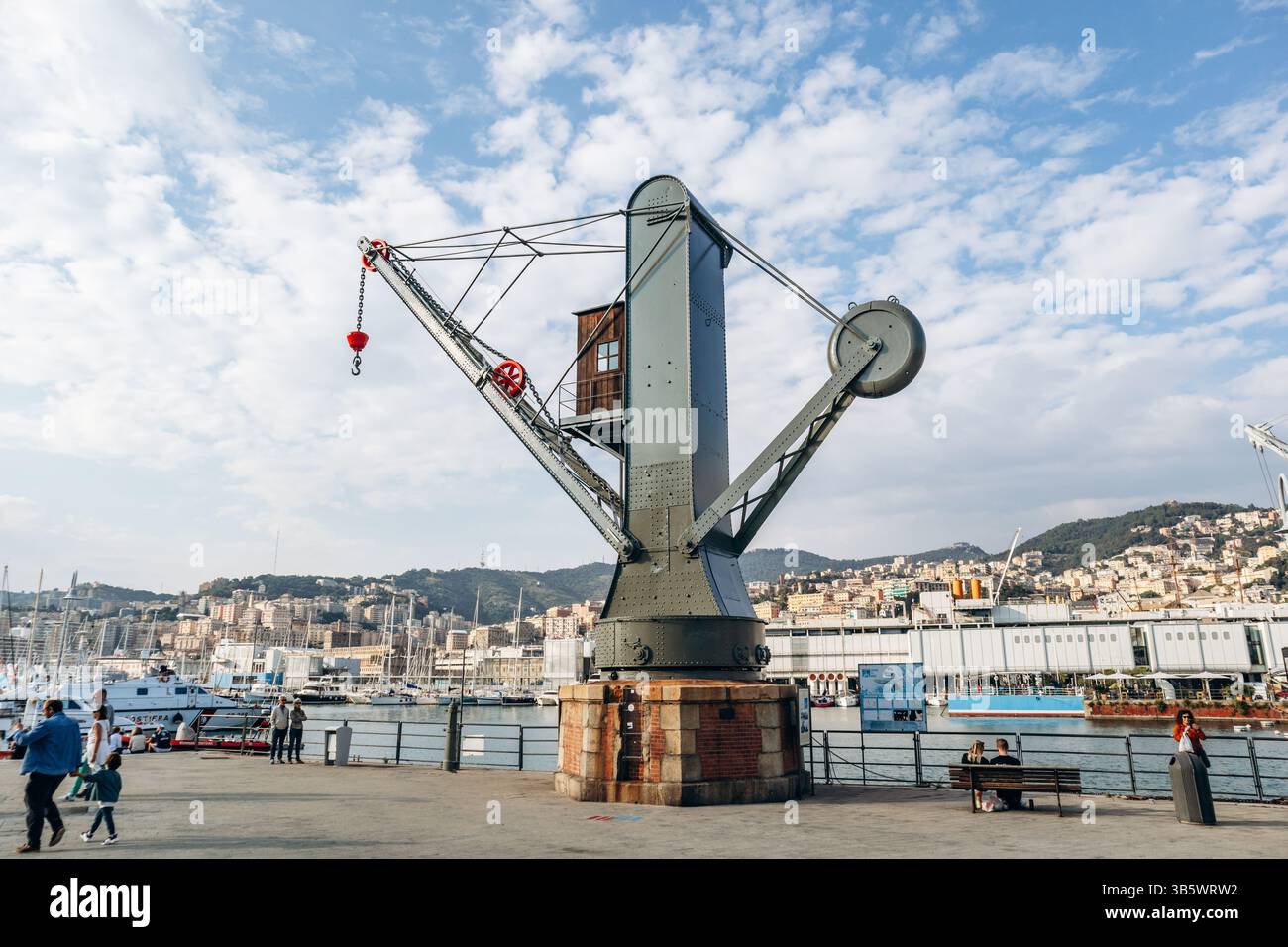 Gênes, Italie - 22 septembre 2024 : grue industrielle historique sur le front de mer du vieux port avec vue sur la ville et la marina. Banque D'Images