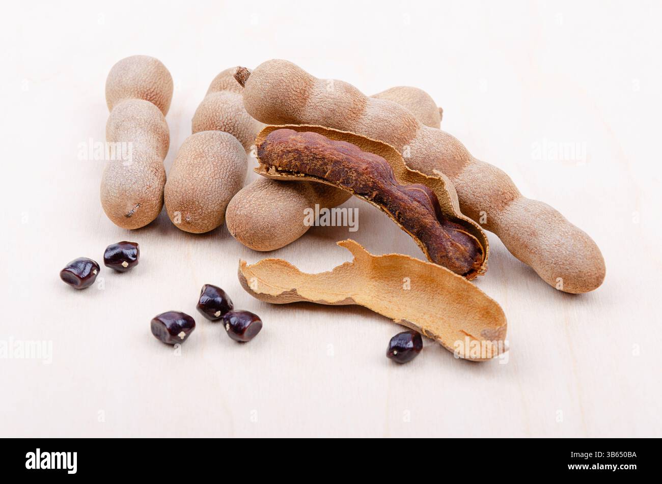 Fruits de tamarin, entiers, cassés ouverts, et graines sur une planche de bois clair. Fruits bruns en forme de gousses de Tamarindus indica, au goût aigre-doux. Banque D'Images