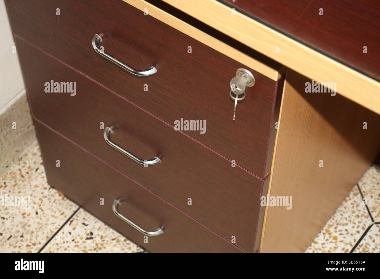 Une vue rapprochée d'un bureau en bois avec trois tiroirs. Les tiroirs ont trois poignées métalliques et celle du haut a une serrure de sécurité avec des clés. Banque D'Images