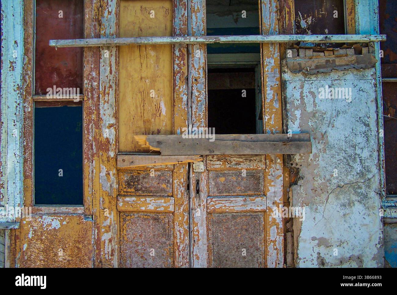 Gros plan d'une porte en bois qui s'effondrait et arborait avec de la peinture fissurée et écaillée dans les tons de jaune, bleu et brun. Banque D'Images