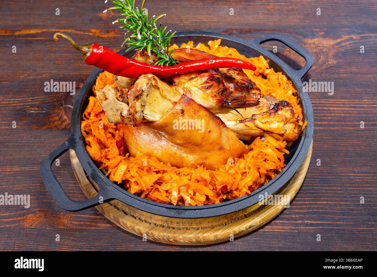 Un jarret de porc délicieusement rôti se trouve au sommet d'un lit de carottes éclatantes et assaisonnées. Les herbes fraîches et un piment donnent de la couleur à la présentation rustique, Banque D'Images