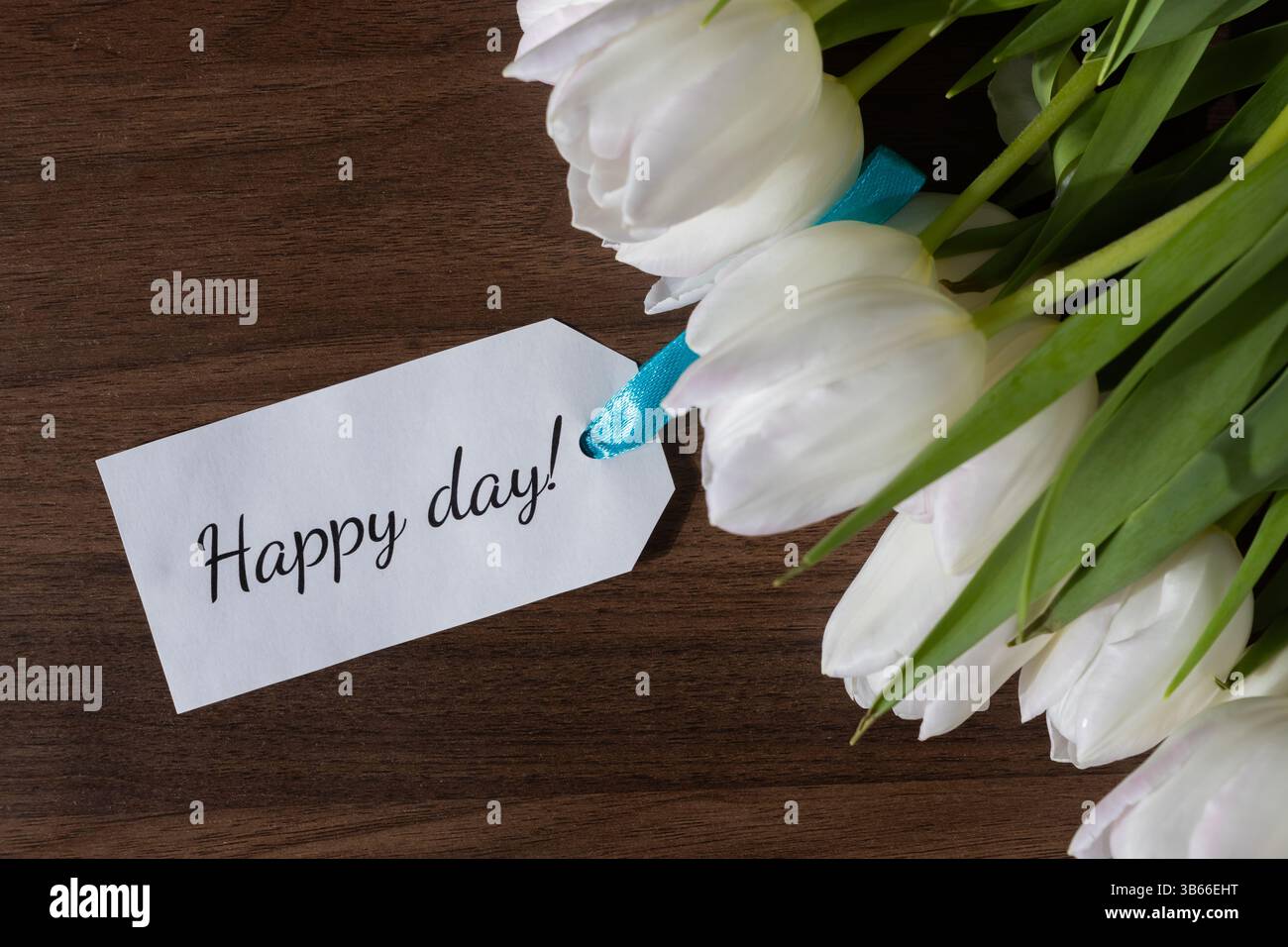 Vue aérienne d'un arrangement de tulipes blanches à côté d'une note de papier de jour heureux, symbolisant les bons voeux et les vibrations positives, parfait pour les cartes de voeux ou ch Banque D'Images