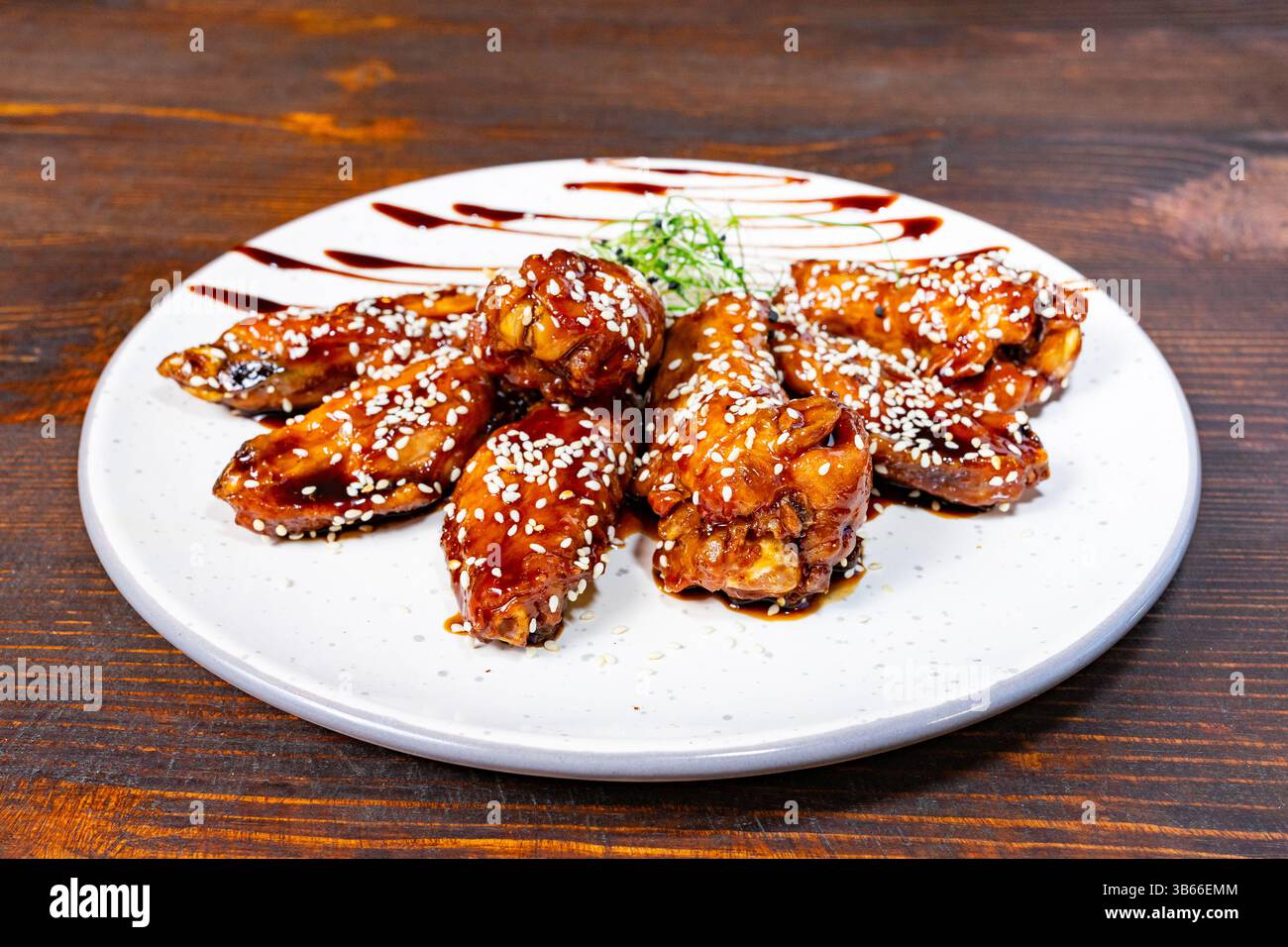 Une assiette contient de délicieuses ailes de poulet glacées saupoudrées de graines de sésame sur une table en bois rustique. Le plat est habilement présenté avec des gouttes de SAU Banque D'Images