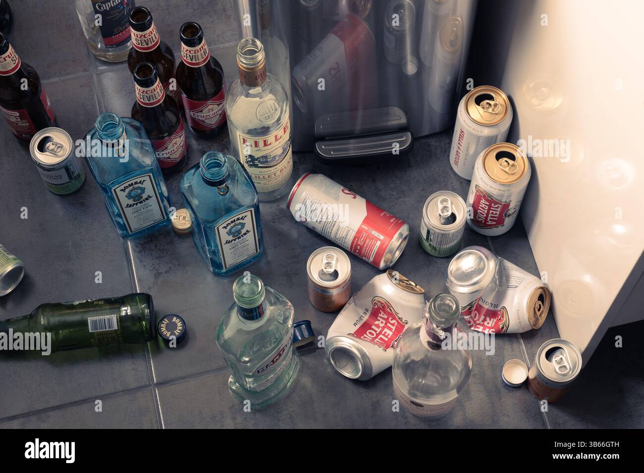 Videz les canettes de bière et les bouteilles de spiritueux sur un plancher de cuisine à côté d'un bac, Angleterre. Concept : alcoolique fonctionnel, alcoolisme, dépendance, vie gaspillée Banque D'Images