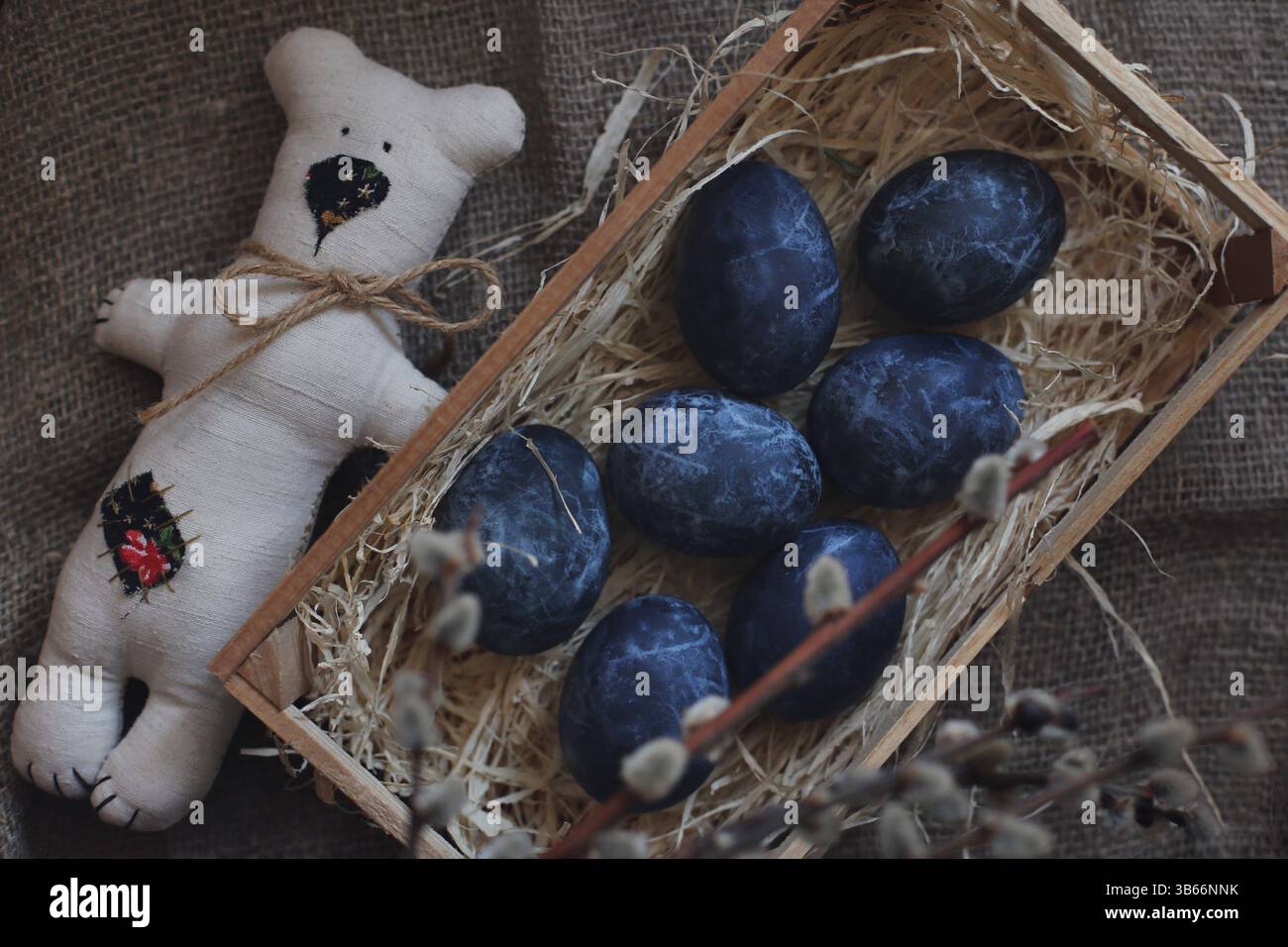 Oeufs de Pâques teints au thé hibiscus, ponte à plat. Oeufs de Pâques bleu foncé teints à la main dans un nid de paille naturel avec un ours en tissu fait à la main, des branches de saule. Banque D'Images