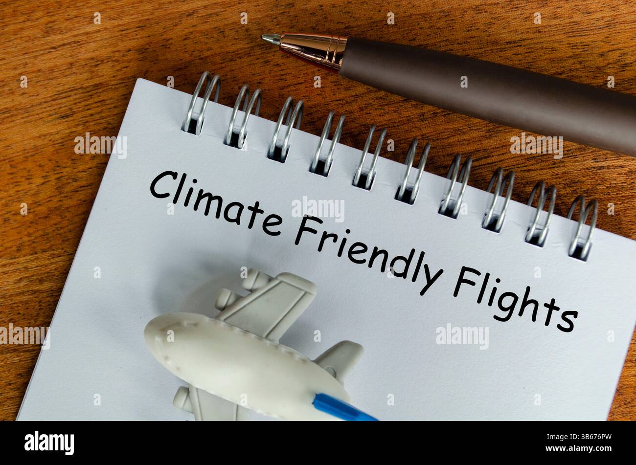 Vue de dessus du texte Climate Friendly Flight sur le bloc-notes blanc avec petit avion et fond de stylo. Sensibilisation à l'environnement. Banque D'Images