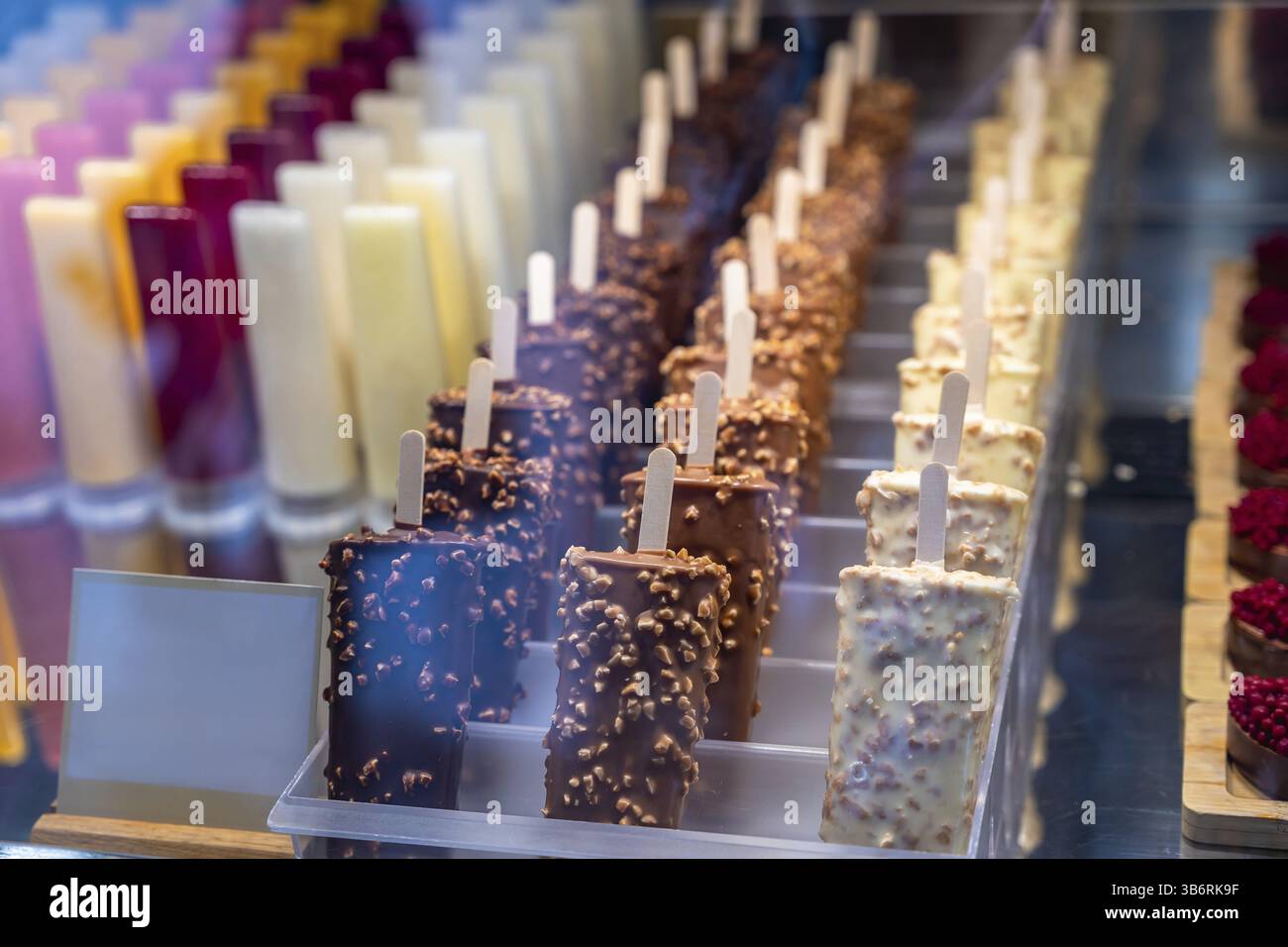 Délicieuses popsicles à la crème glacée avec enrobage de chocolat et de noix affichées en rangées dans une vitrine Banque D'Images