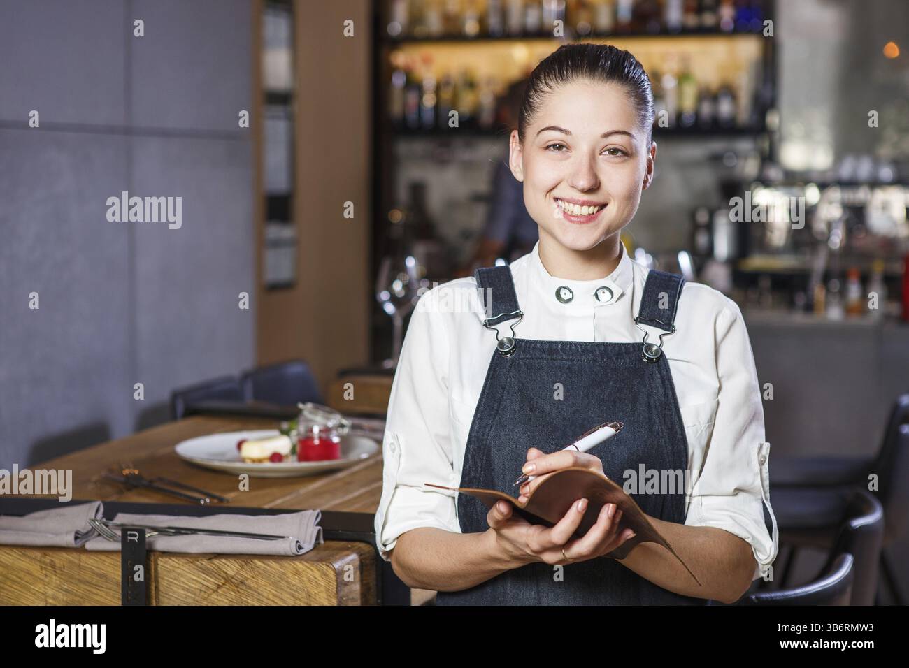 Ganson, dirigeants, belle deushka avec un sourire et des cheveux en forme de travail recueillies apron accepte une commande dans un restaurant près du desservie w Banque D'Images