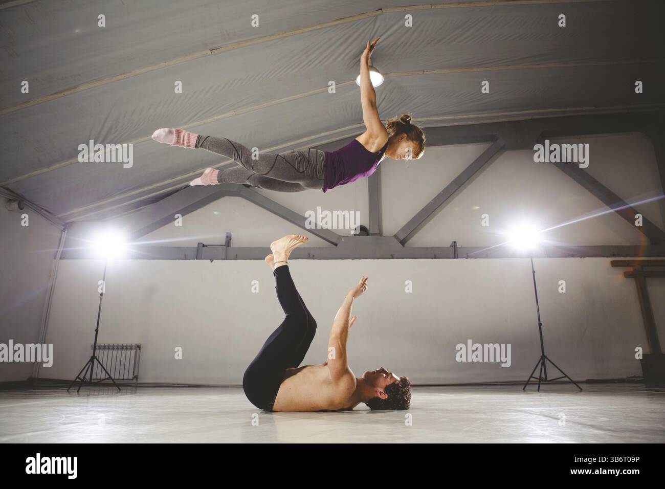 Le thème de l'Acroyoga et postures de yoga. Acroyogis. pratique avec rétro-éclairage studio. l'homme de base lance la femme Pop Flyer en vol jusqu'. Acr Position Banque D'Images
