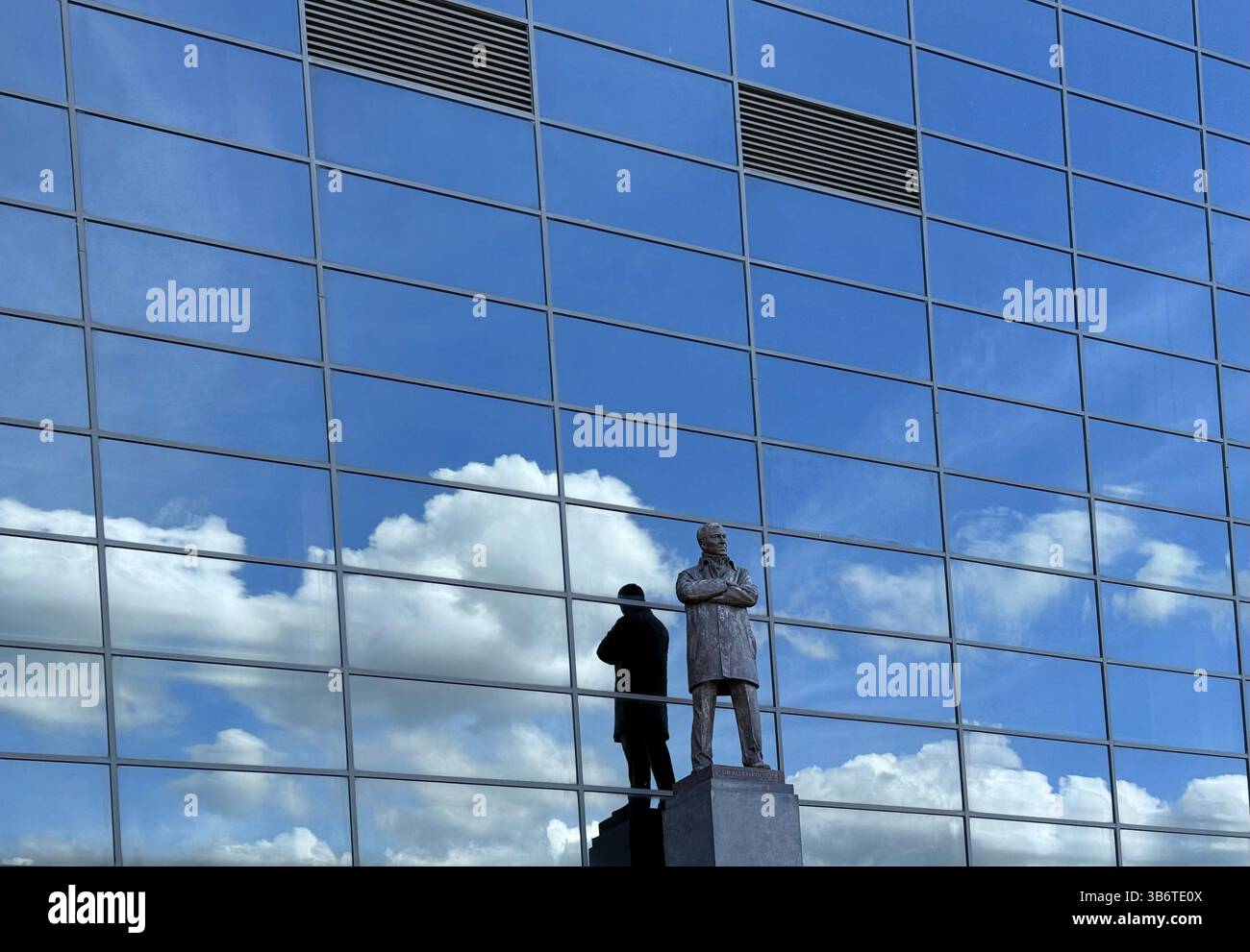Sir Alex Ferguson Stand au stade de football Old Trafford. Statue avec nuages et ciel bleu reflété dans les fenêtres de stand. Manchester, royaume-uni - Image de stock capturée avec un smartphone