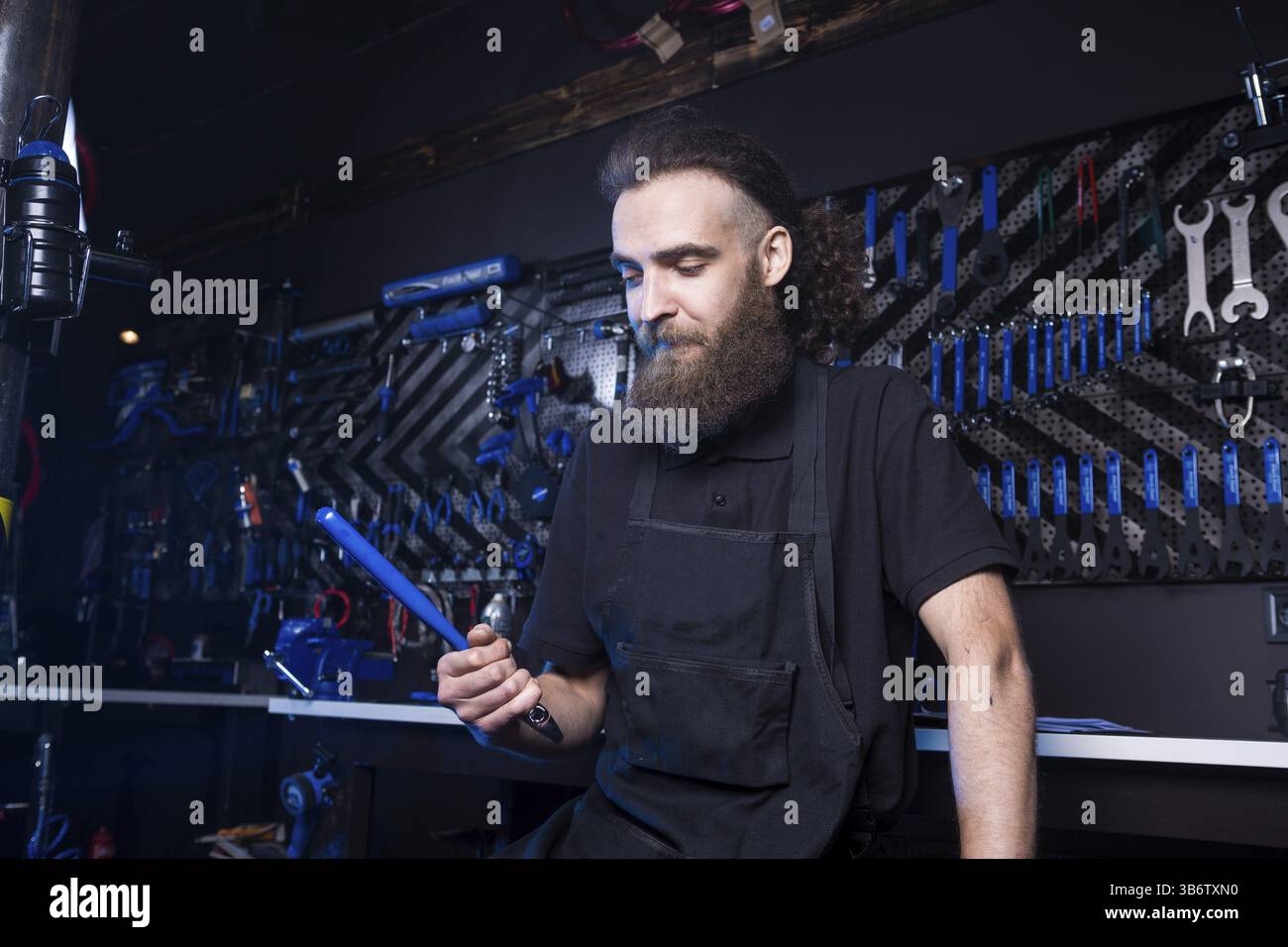 Portrait de propriétaire de petite entreprise de jeune homme à la barbe. Guy atelier mécanicien vélo worker sitting avec l'outil dans sa main dans un vetement noir Banque D'Images