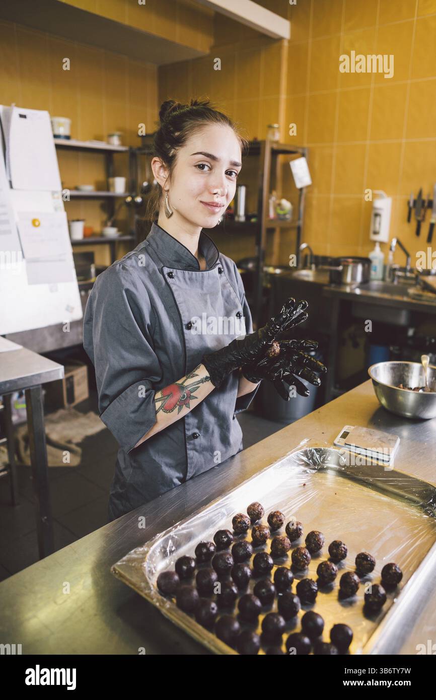 Sujet profession et la cuisson de la pâte. young Caucasian woman with tattoo de chef pâtissier dans un restaurant de cuisine la préparation de bonbons au chocolat ronde han Banque D'Images