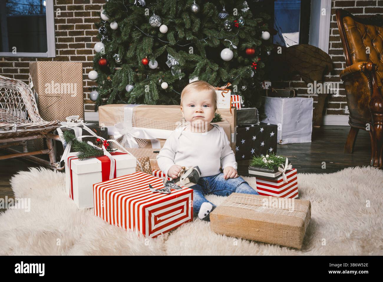 Thème hiver et vacances de Noël. Enfant garçon caucasien blond 1 an assis à la maison près de l'arbre de Noël avec décor du nouvel an sur tapis shaggy Banque D'Images