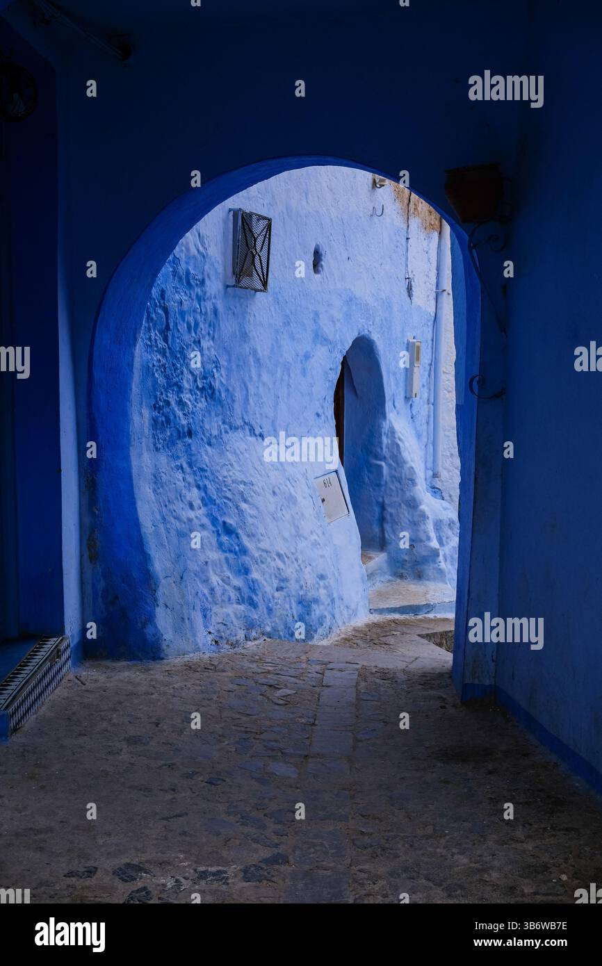 Une ruelle sereine et lavée au bleu à Chefchaouen, Maroc, avec une porte rustique encadrée par une arche, vous invitant à explorer le charme caché de la ville. Banque D'Images
