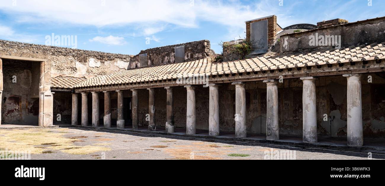 Ruines d'un ancien bâtiment romain avec des colonnes et un toit de tuiles, présentant des murs altérés et une architecture historique sous un ciel bleu. Banque D'Images