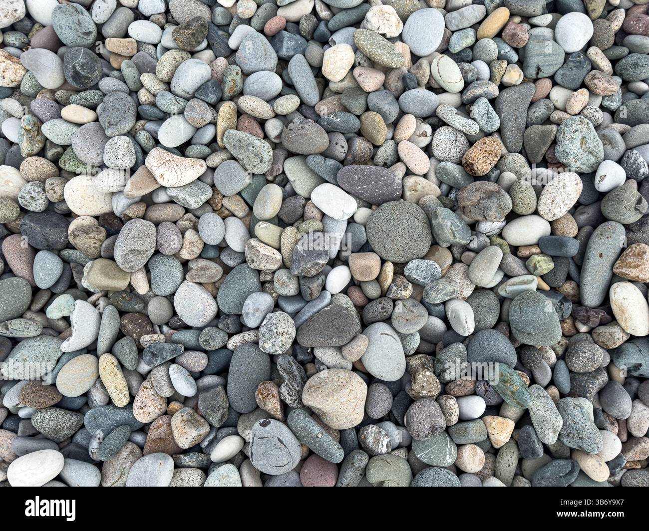 Vue de dessus de galets mélangés lisses sur une plage naturelle. Texture côtière et fond abstrait, pas de personnes, voyage et thème de la nature. Banque D'Images