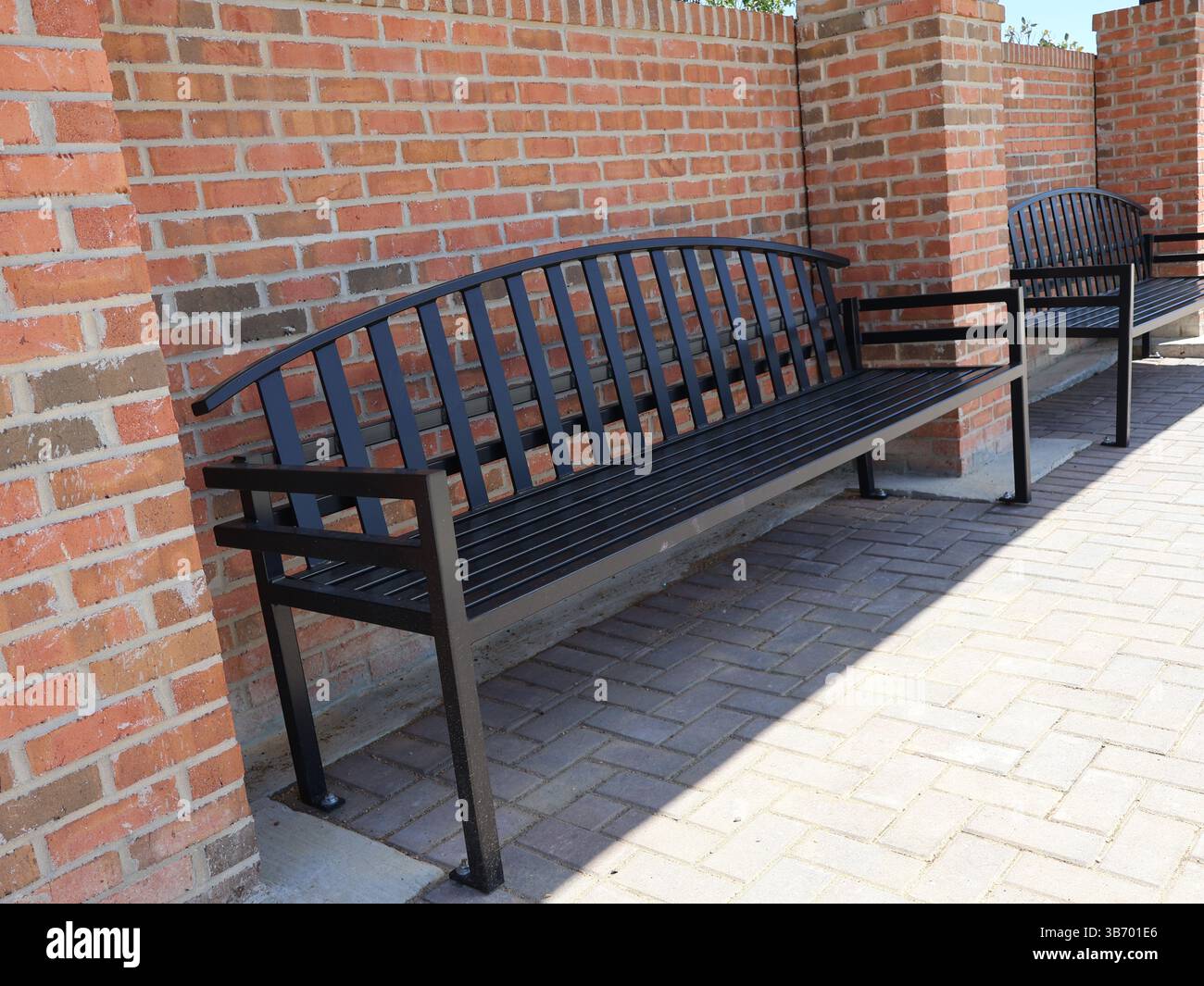 bancs en métal noir avec sièges à lattes et dossiers ancrés à des pavés de briques près de briques rouges dans un motif de maçonnerie traditionnel avec une vue rapprochée de th Banque D'Images bancs en métal noir avec sièges à lattes et dossiers ancrés à des pavés de briques près de briques rouges dans un motif de maçonnerie traditionnel avec une vue rapprochée de th Banque D'Images