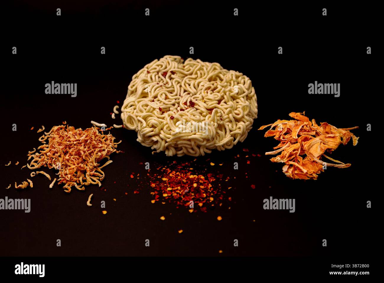Ingrédients bruts pour nouilles ramen préparation - nouilles de blé entourées d'oignon déshydraté, de carotte et de piment broyé sur fond noir. Banque D'Images