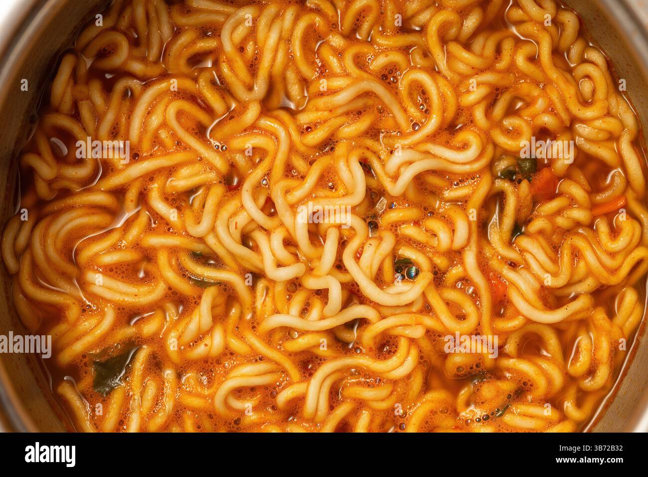 Gros plan de nouilles ramen instantanées fraîchement cuites immergées dans un riche bouillon rouge orangé, épicé au Chili. Banque D'Images