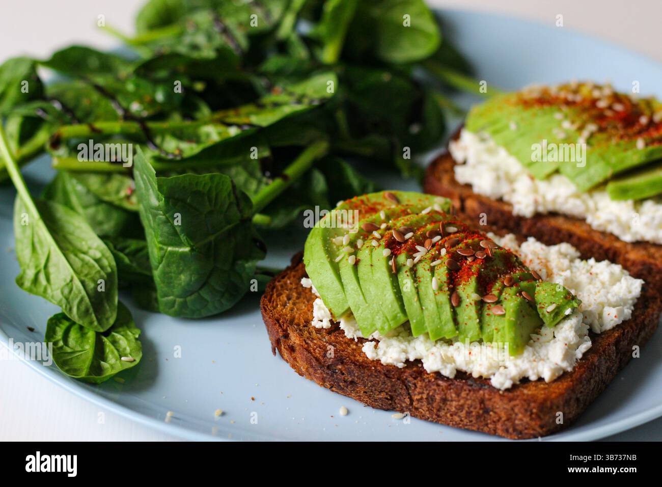 Toast de seigle avec fromage cottage, avocat, sésame, graines de lin, paprika fumé et poivre. Servi avec épinards frais, jus de citron, huile d'olive et balsamique Banque D'Images