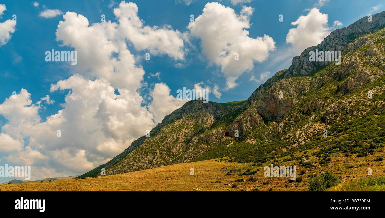 Prairie dorée et contreforts parfumés au thym s'élevant à des falaises de calcaire déchiquetées percées de grottes cachées dans la région albanaise de Prespa sous un nuage dispersé Banque D'Images