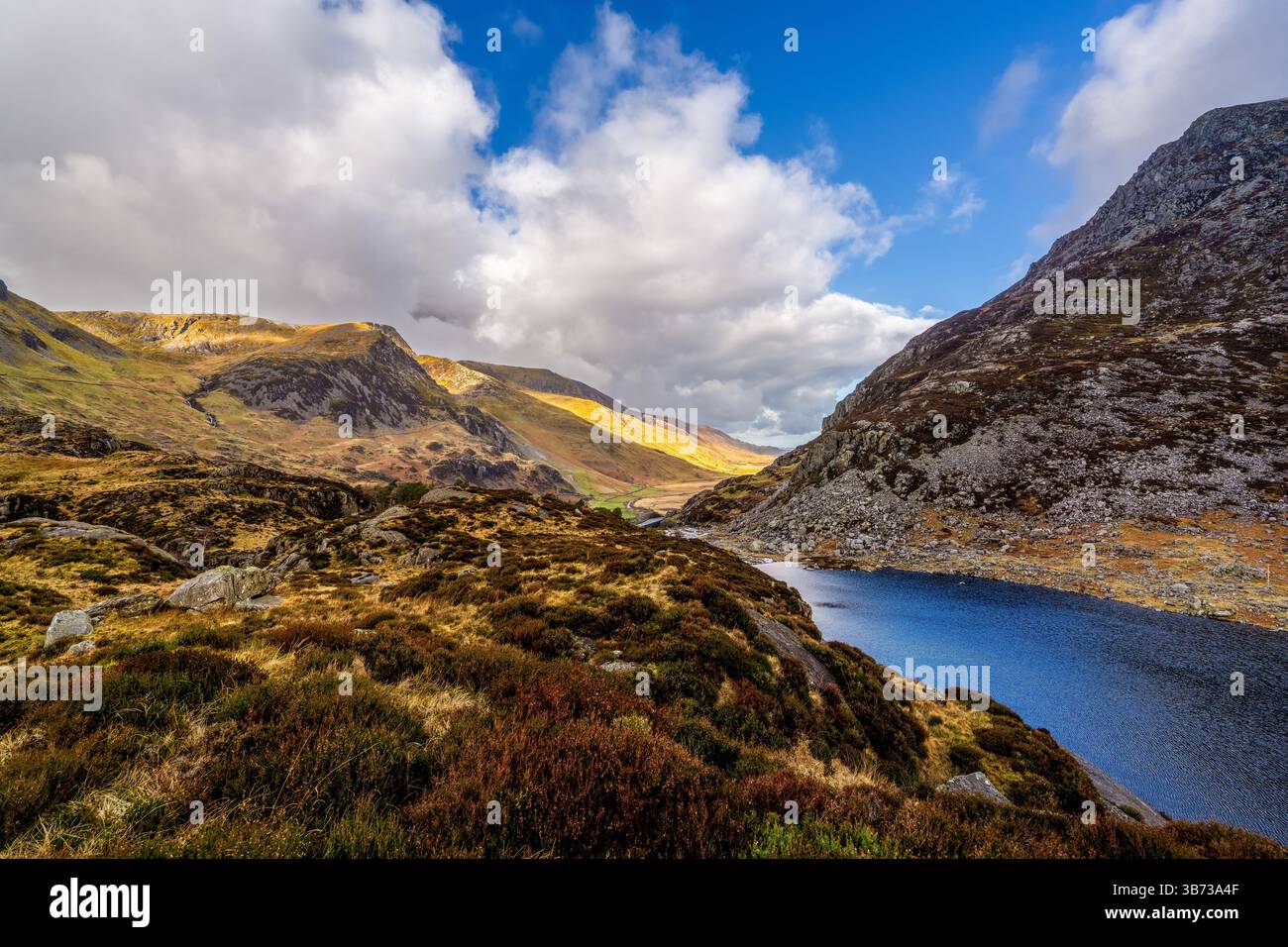 Sunlit Llyn Idwal niché au pied de pentes abruptes et de landes balayées par le vent sous une spectaculaire banque de cumulus nuages Banque D'Images
