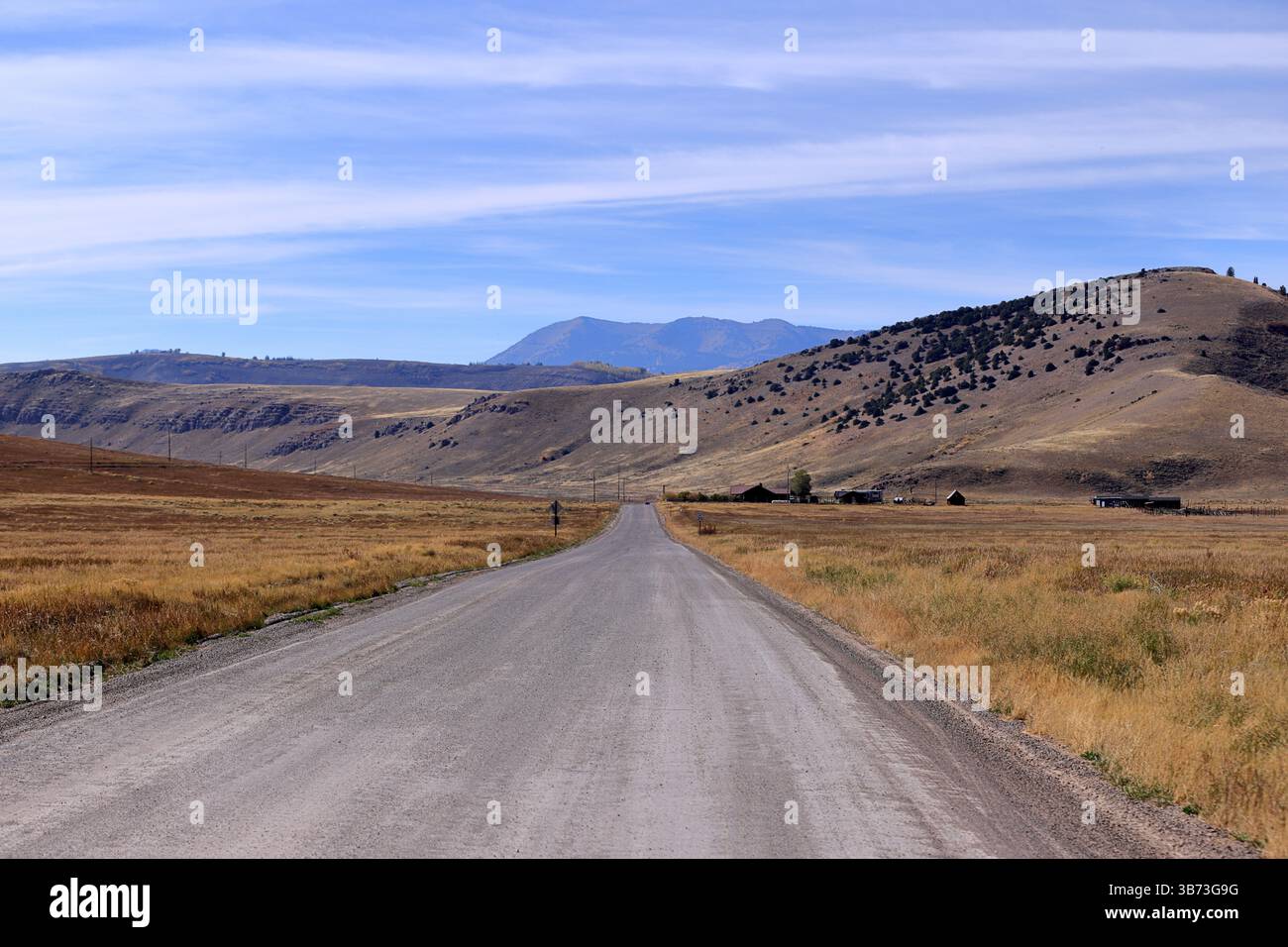 Dans le parc national de Grand Teton, Wyoming, une route droite serpente le long de prairies vives, de granges rustiques et de pics imposants, couronnés par des nuages dérivants pour l'automne. Banque D'Images