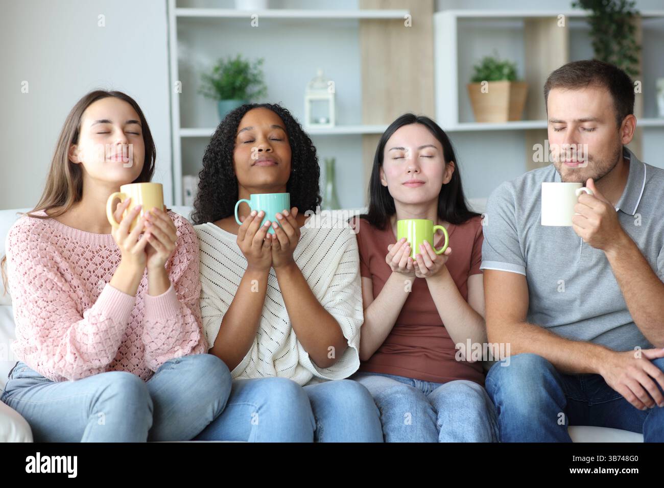 Groupe de quatre amis sentant des boissons assis sur un canapé à la maison Banque D'Images