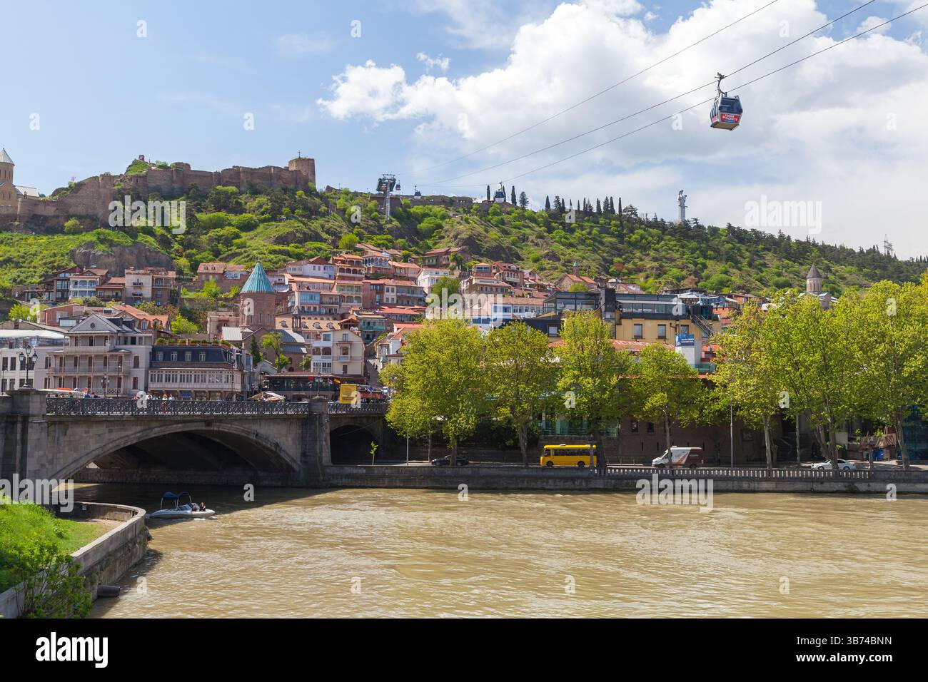 Tbilissi, Géorgie - 29 avril 2019 : un paysage urbain pittoresque avec des bâtiments colorés le long d'une rivière, une végétation luxuriante sur les collines, et un téléphérique dans le Banque D'Images