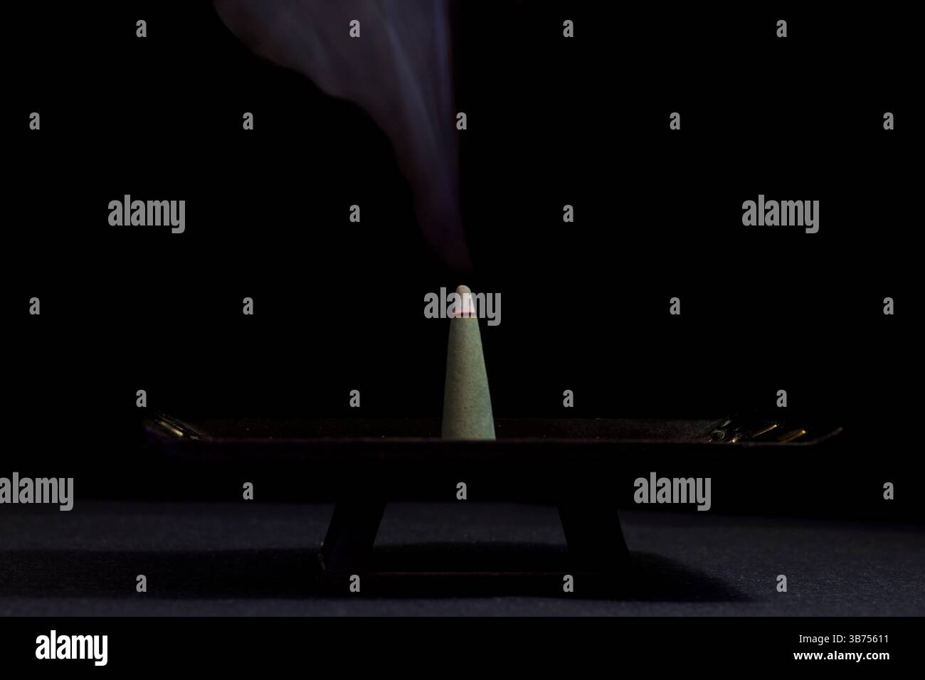 Cône d'encens allumé avec de la fumée aromatique sur un fond horizontal noir Banque D'Images