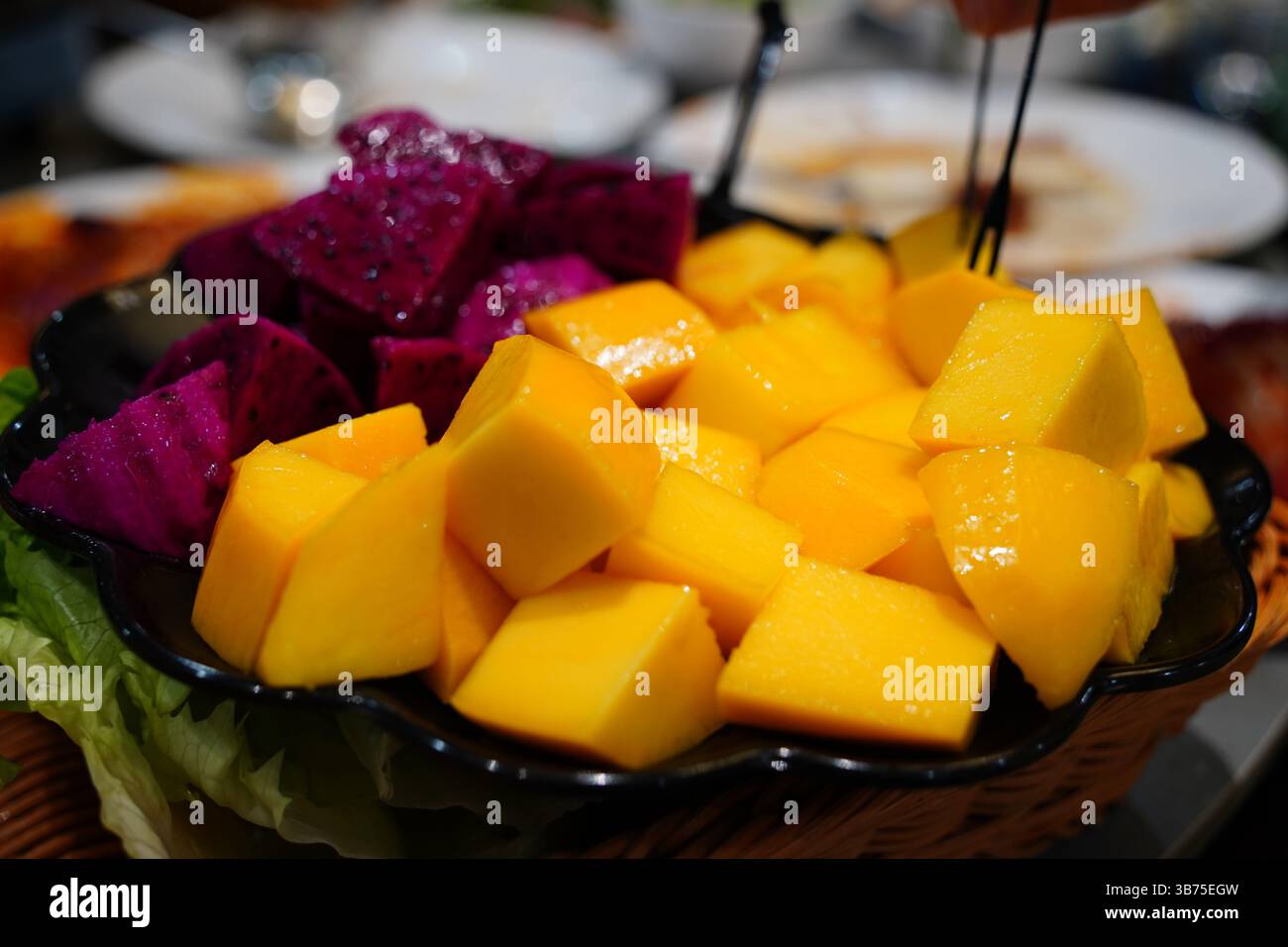 Gros plan de mangue fraîche en cubes et de fruits du dragon sur une assiette sombre – plateau de fruits tropicaux Banque D'Images